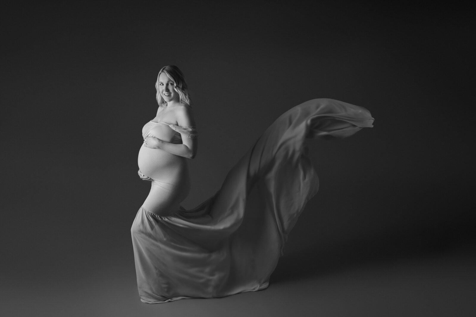 Fine art Maternity Photography Charlotte NC black and white portrait of a light skinned mom to be with light blonde hair, dress train flowing up behind her as if caught by wind.
