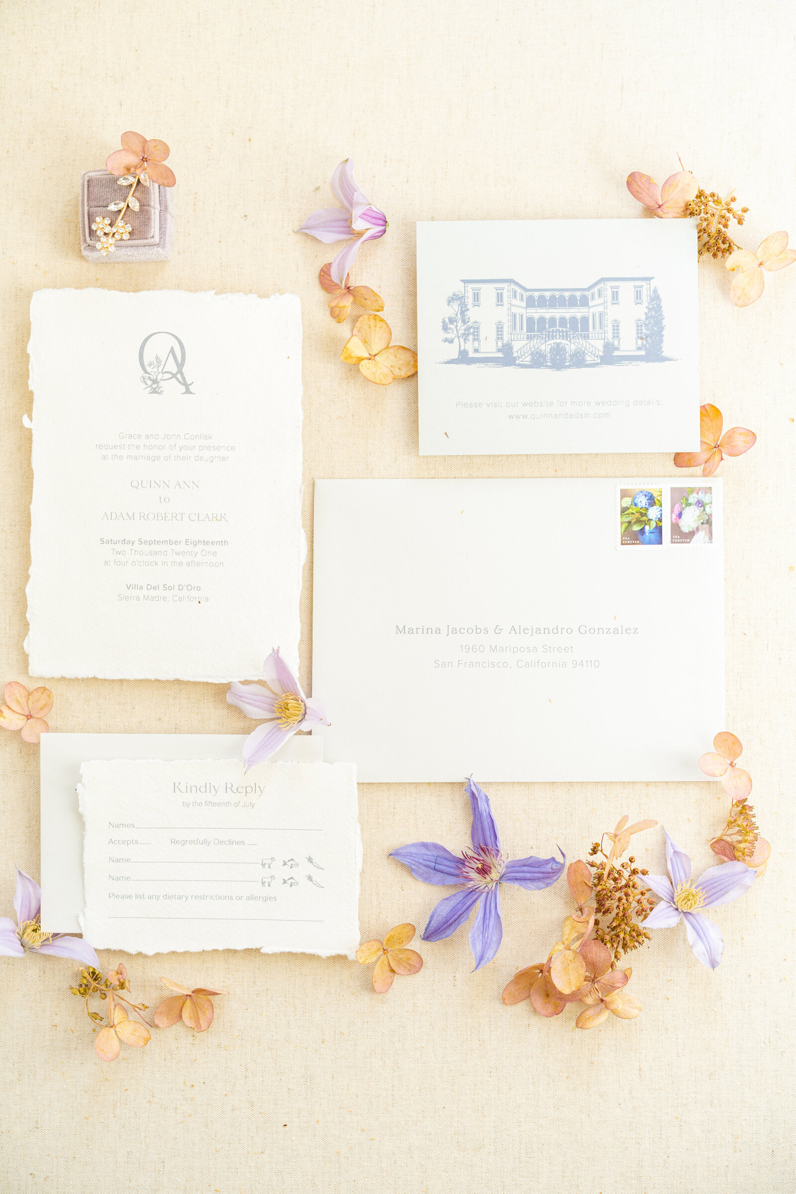 Wedding stationery on white card stock with gray font, flowers and earrings set atop a cream background.