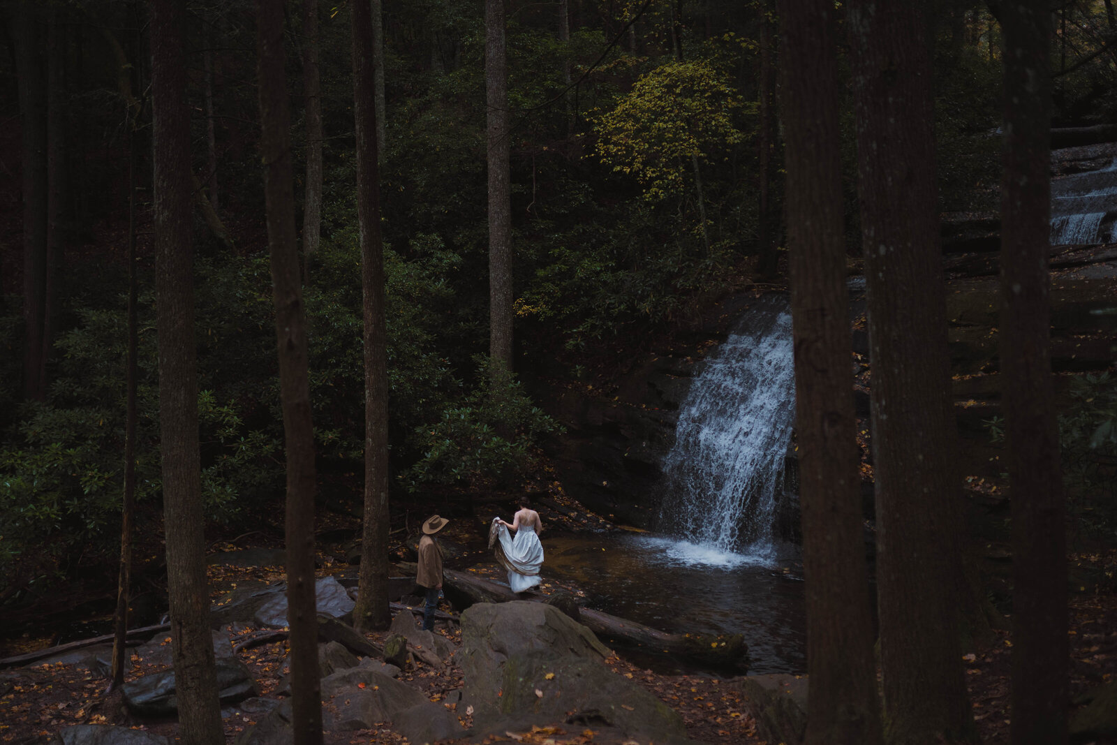 A bride and groom hold hands while looking at the beautiful mountains in the distance at sunset