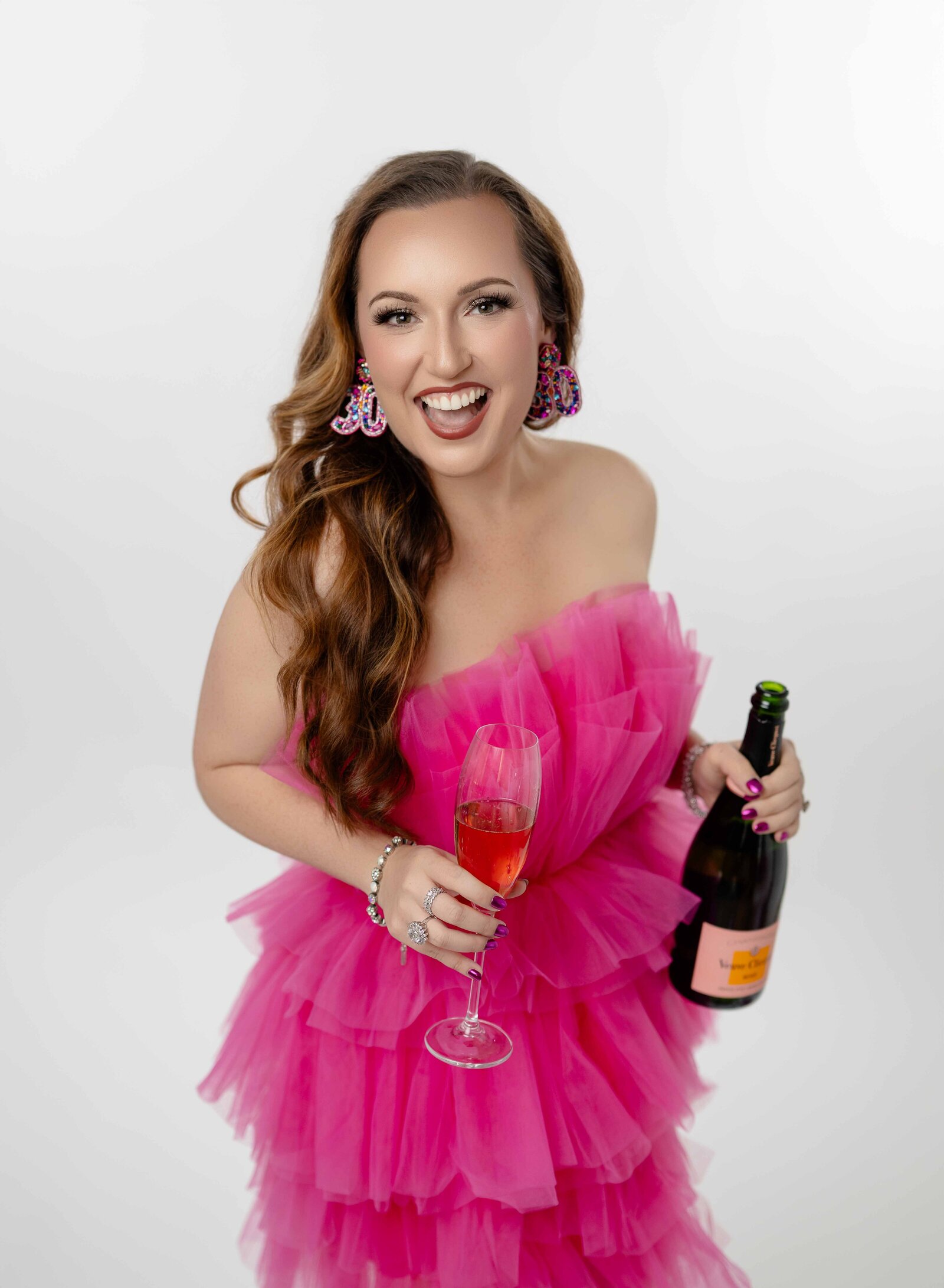 Women in a hot pink dress celebrating her 30th birthday and holding a champagne bottle and flute. Photo taken at Atlanta Birthday photo studio.