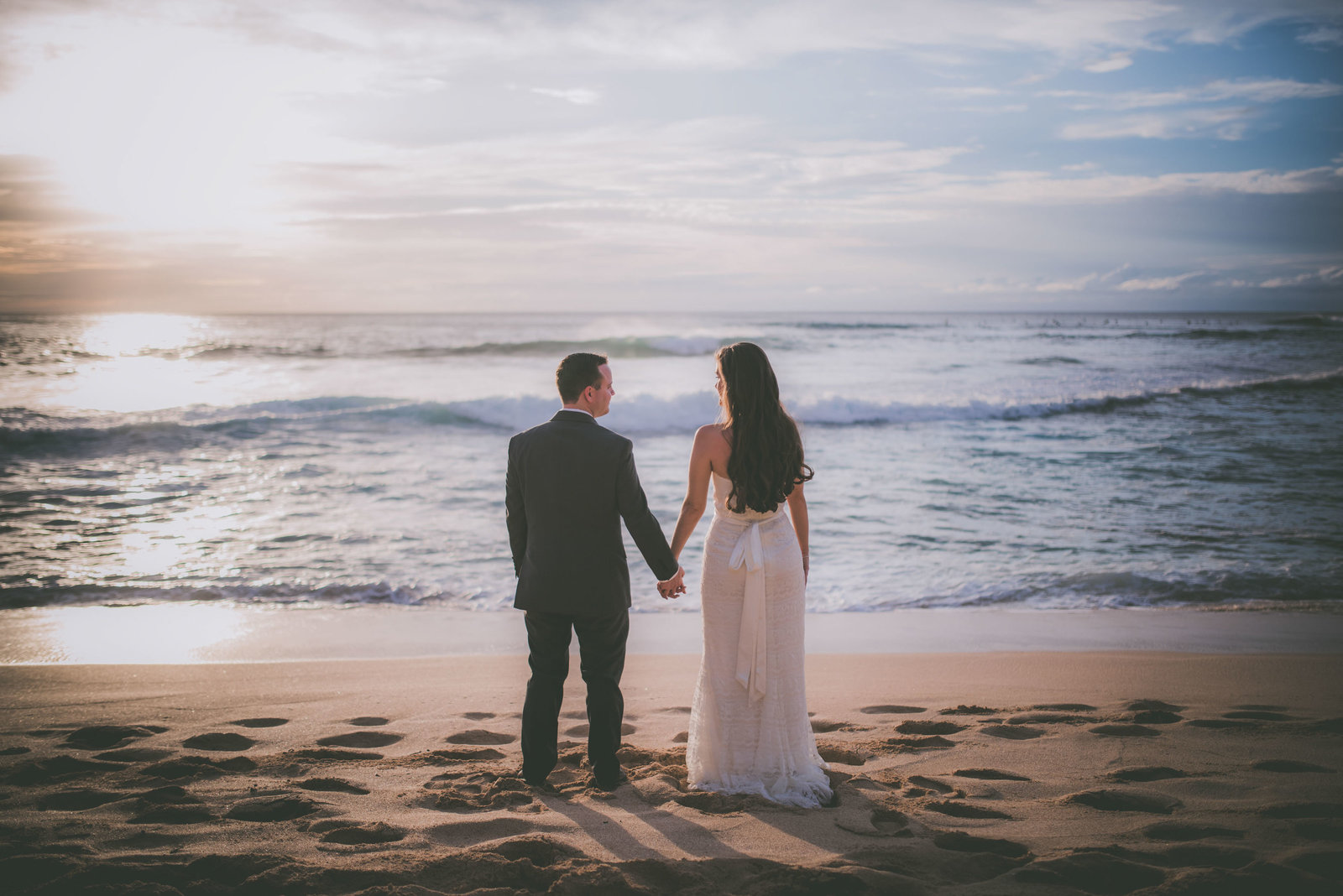 Oahu couple holds hands on beach during sunset.