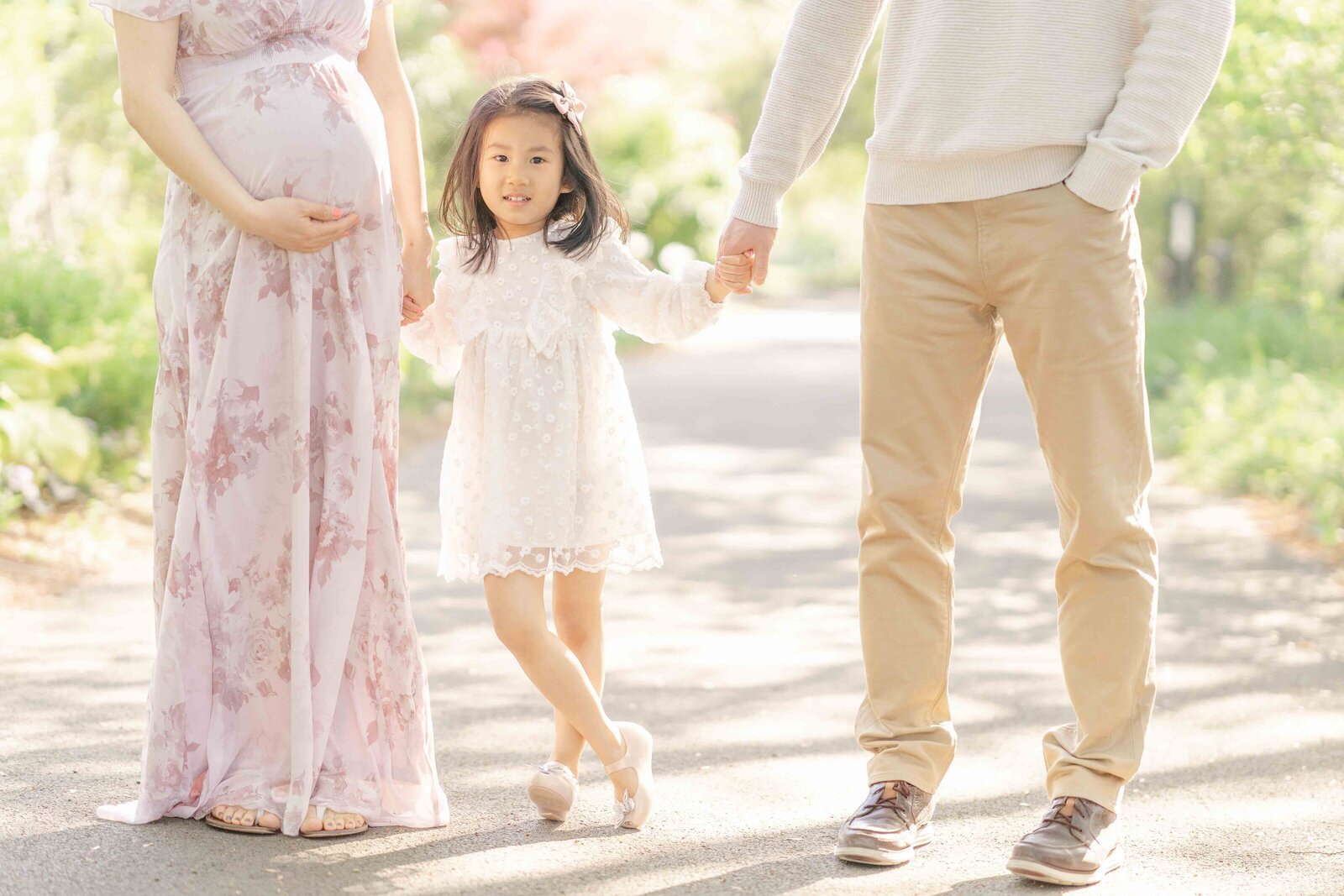 big sister holding parents’ hands during Ashburn, Virginia maternity picture