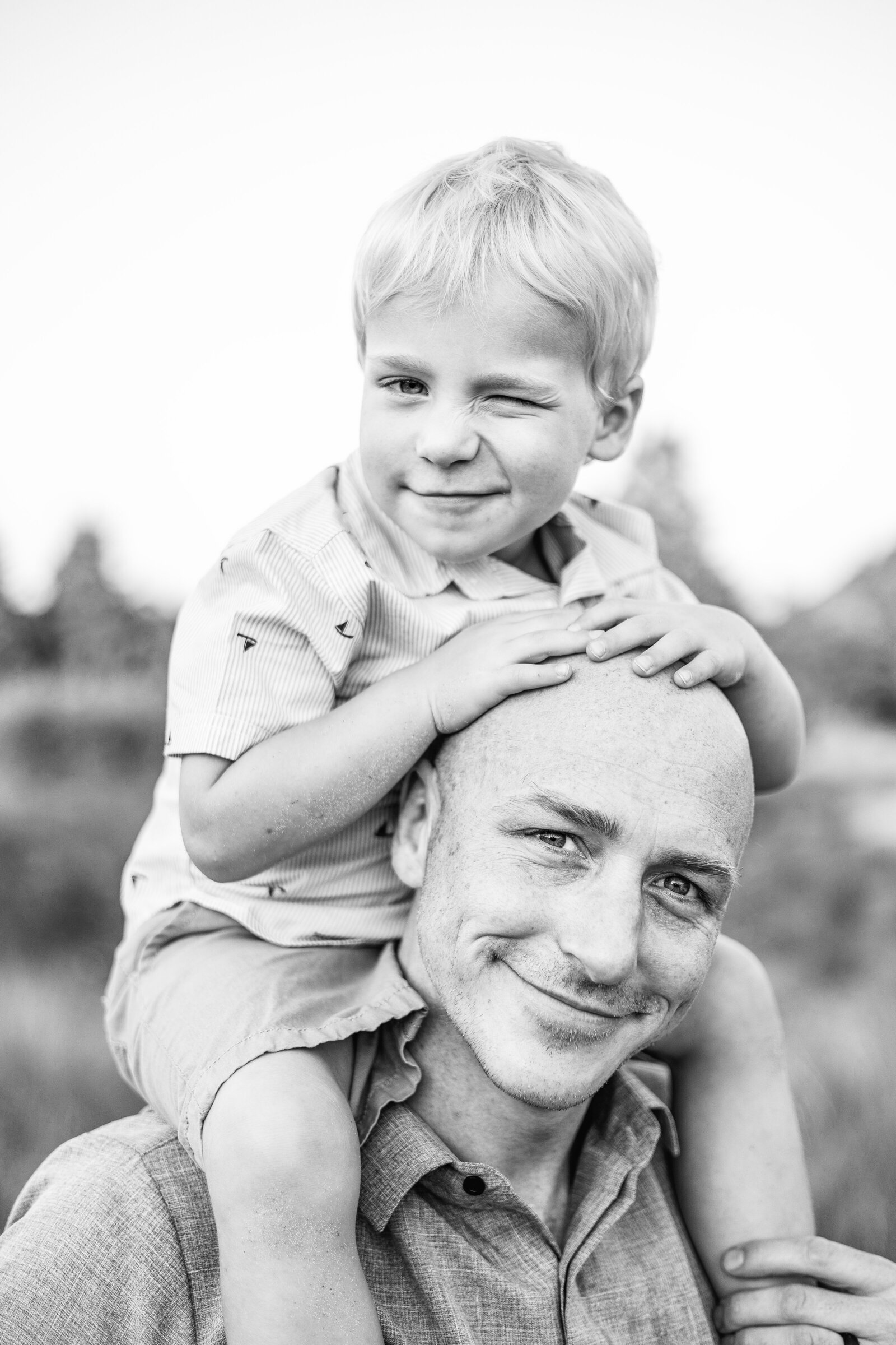 A joyful black-and-white portrait of a father carrying his smiling son on his shoulders in Grand Rapids, Michigan, capturing their playful and loving bond.