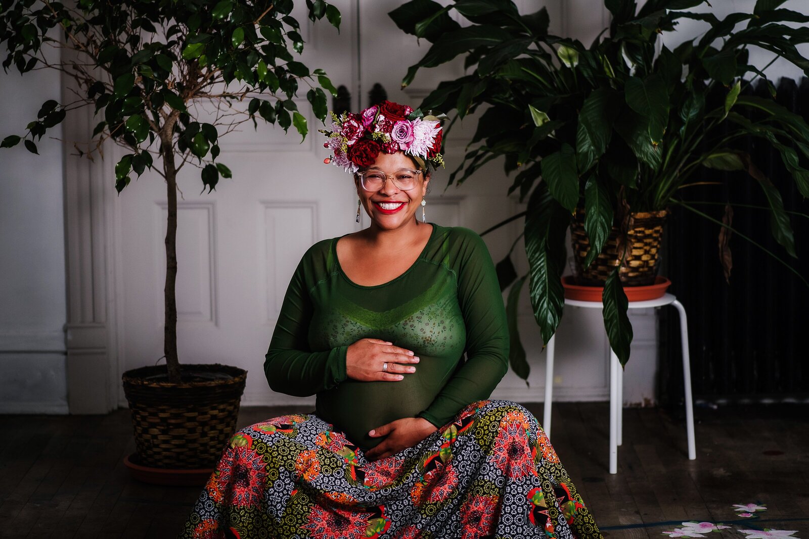 Mom in flower crown and colorful skirt, surrounded by plants holding belly and smiling. Maternity photo
