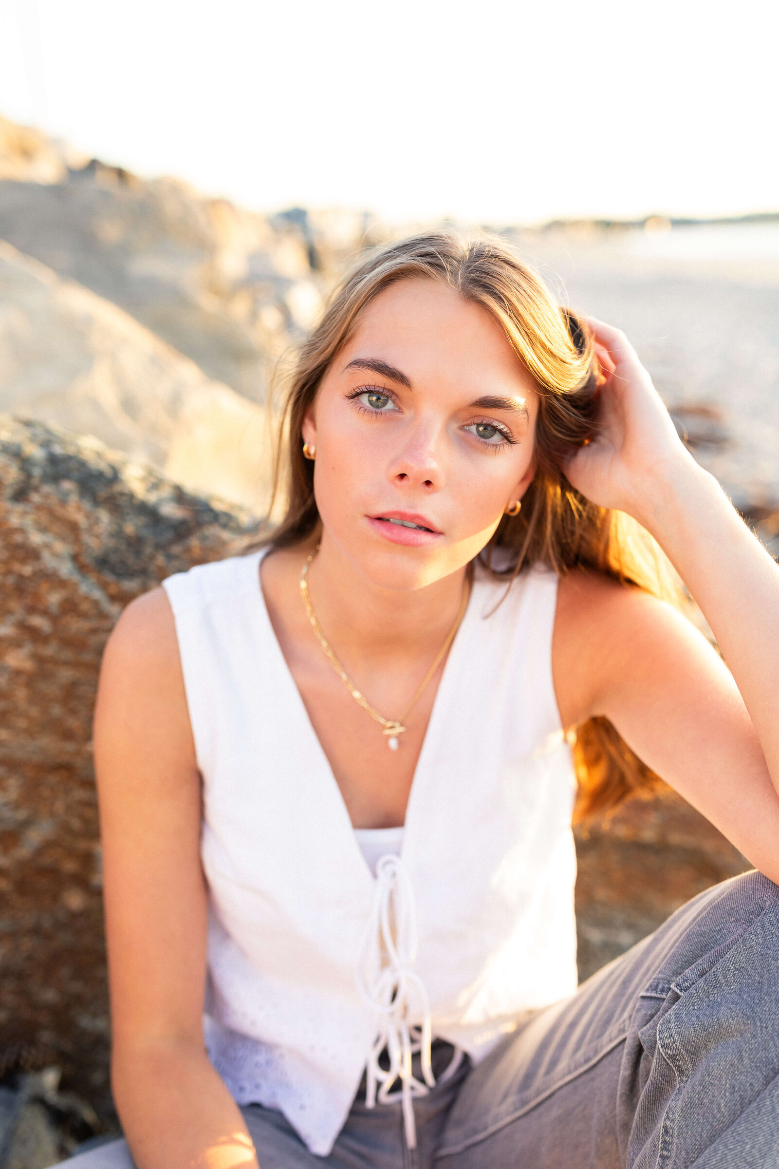 brunette high schooler posing on a beach wearing a white shirt