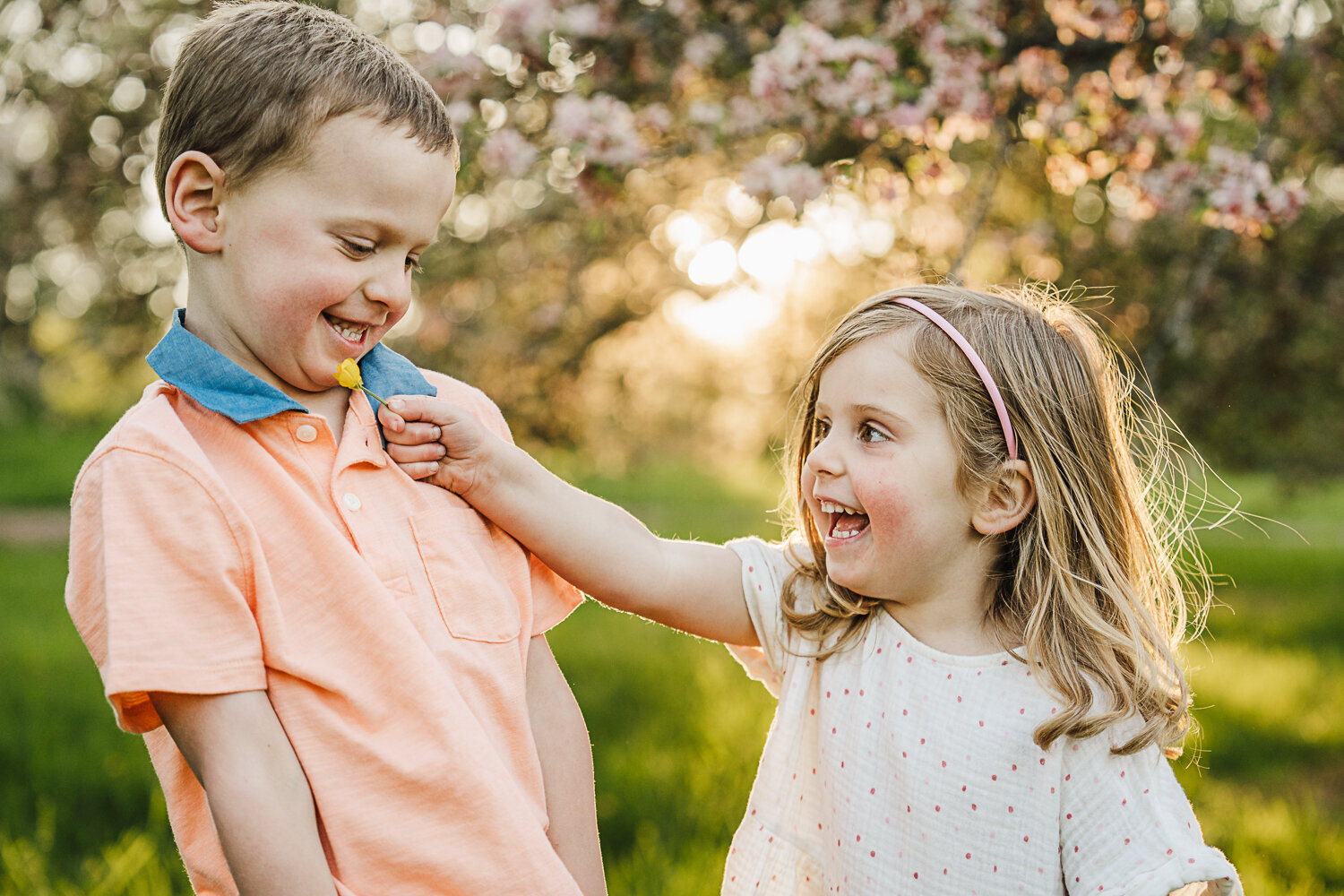 two kids laugh together under blossoming trees at sunset