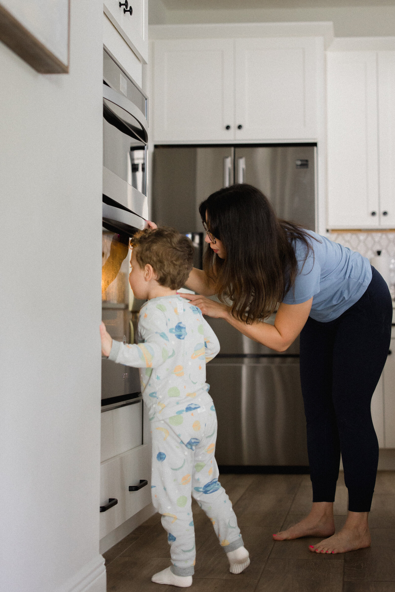 Mom and son look into oven to watch muffins baking beneath a glowing light