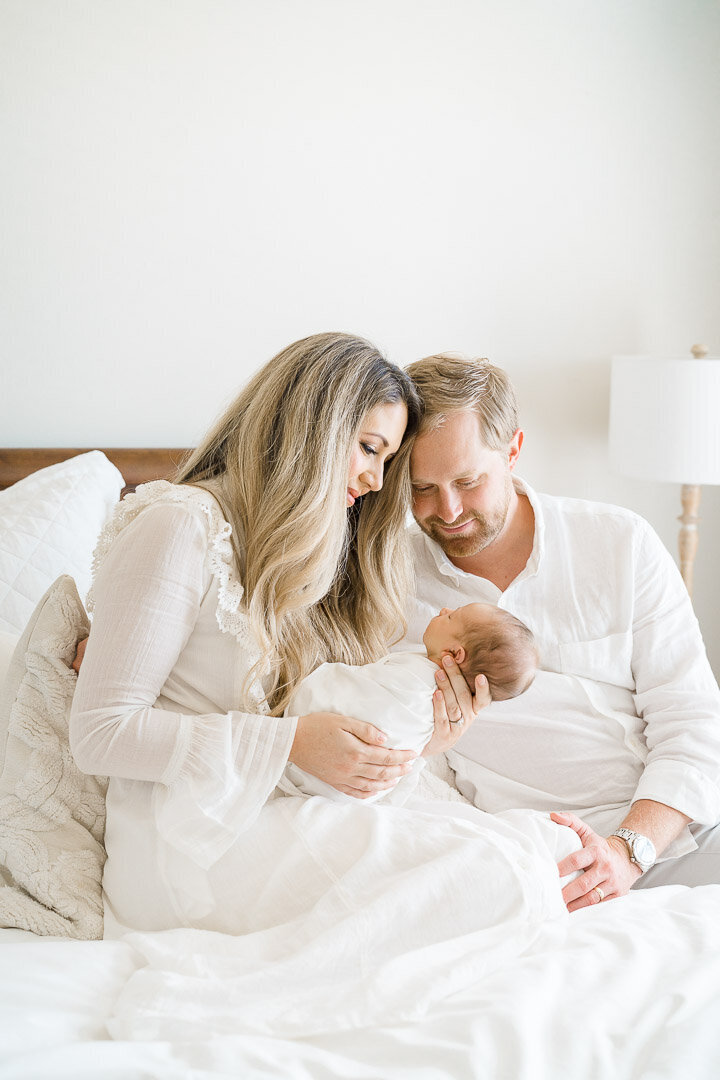 Mom and Dad dressed in white hold newborn baby