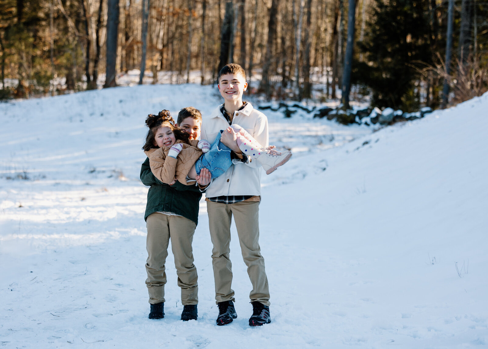 Two brothers hold younger sister during their family photo session in Lee, New Hampshire