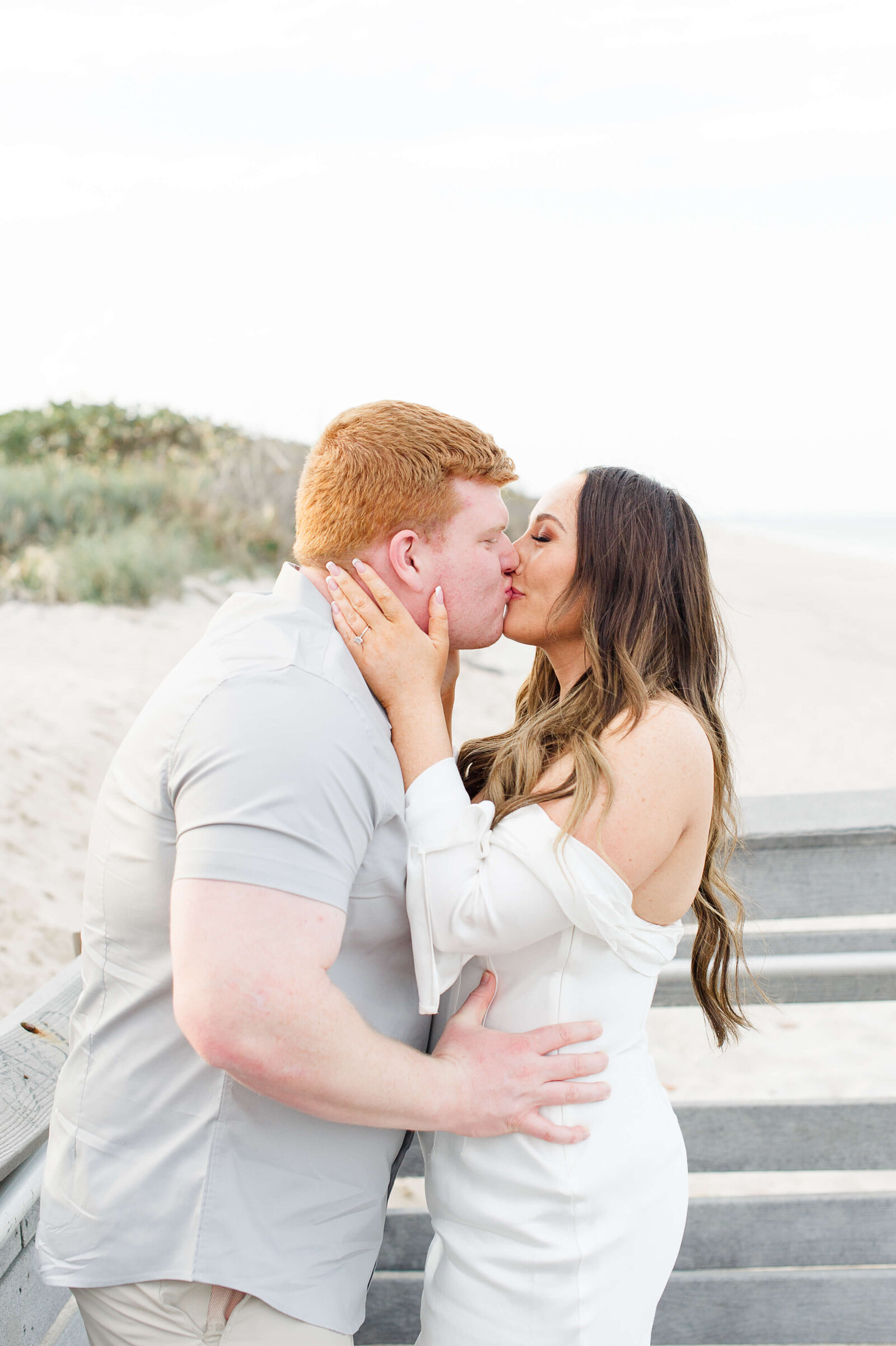 Couple stands on the beach kissing during their engagement session with Orlando engagement phtographer M. Lauren