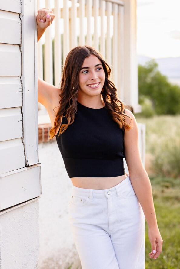 Senior girl poses next to white house at Fly N B park in Highlands Ranch, Colorado.