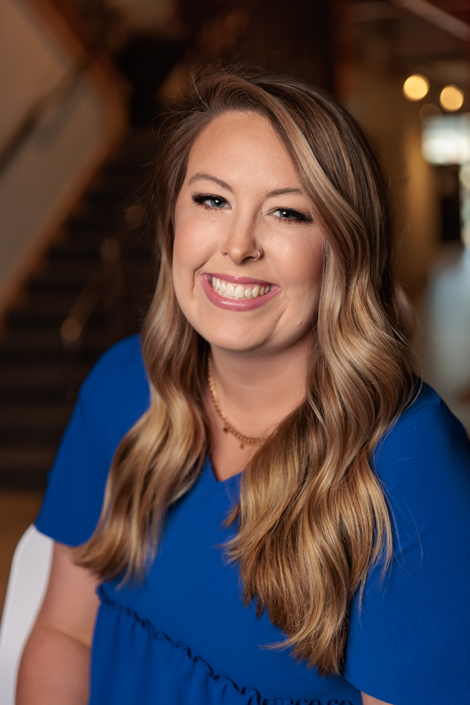 Professional headshots sitting with stairs and lights behind her near Raleigh, NC.
