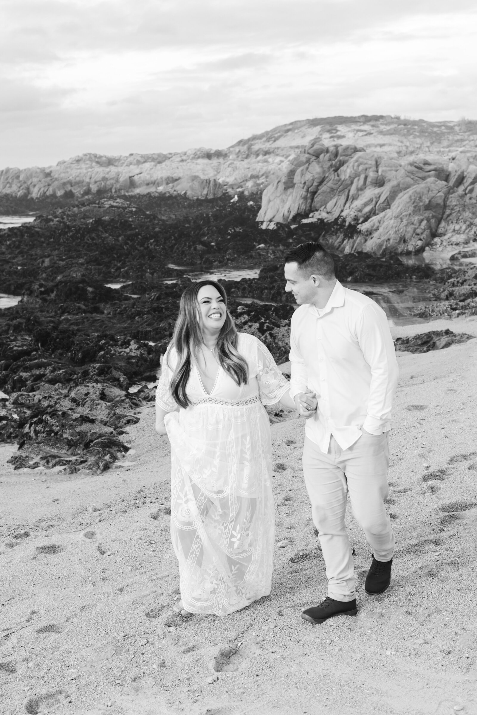 An engaged man and woman take photos on the beach in Pacific Grove, Monterey, California near Big Sur.