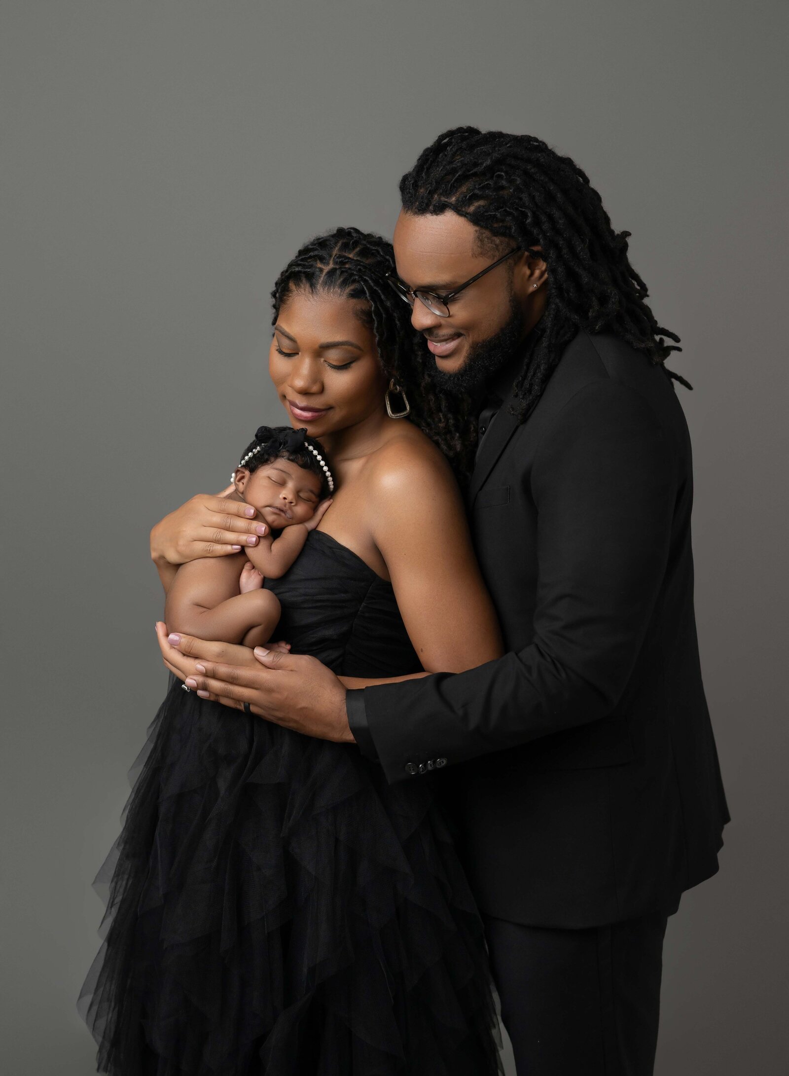 Family of 3 taking newborn family portraits. Baby is naked on Mom's chest and Mom and Dad are dressed in black, looking at baby girl. Photographed by Jenni Nikki Photography at Marietta Newborn Photo Studio.