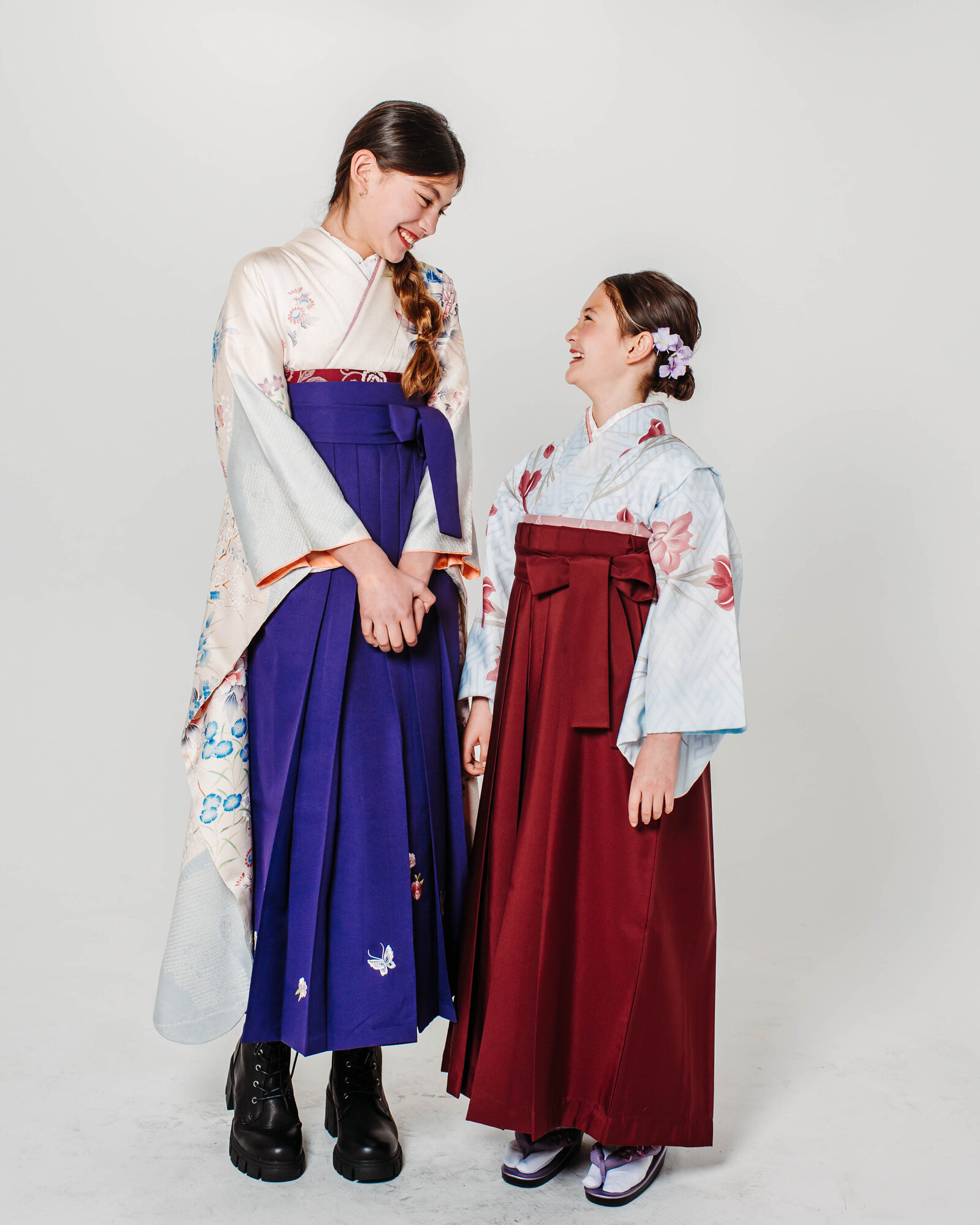 Two girls in colorful hakama standing and smiling at each other for graduation portrait | 卒業式 カラフルな袴姿で見つめ合い笑顔を見せる二人の女の子
