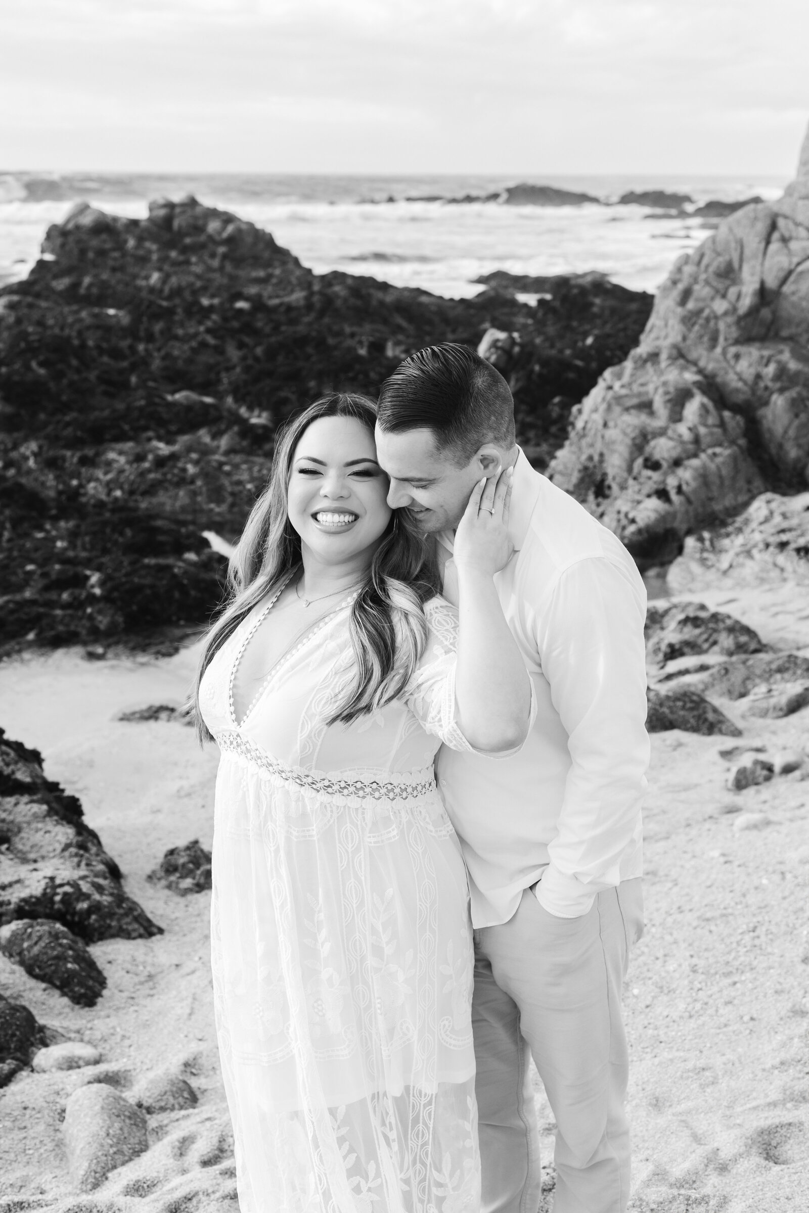 An engaged man and woman take photos on the beach in Pacific Grove, Monterey, California near Big Sur.