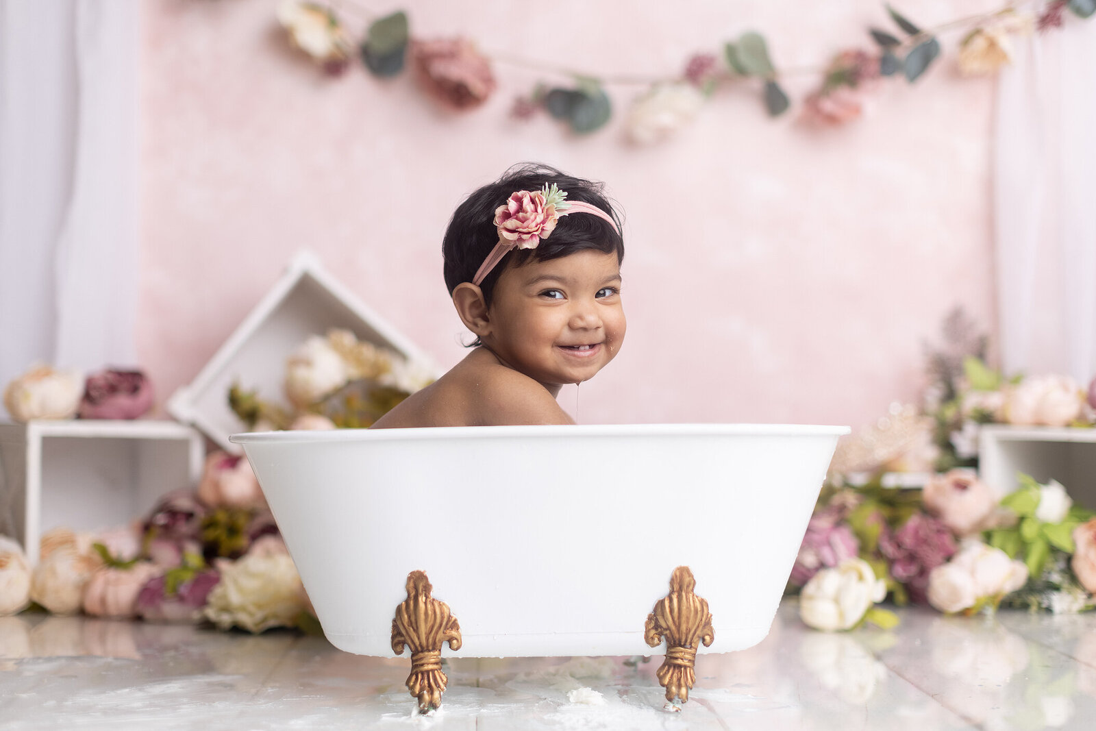 Girl splashes in tub at her first birthday photoshoot.