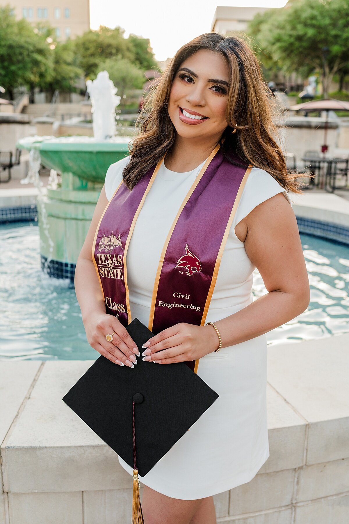 Texas State grad standing by fountain 
