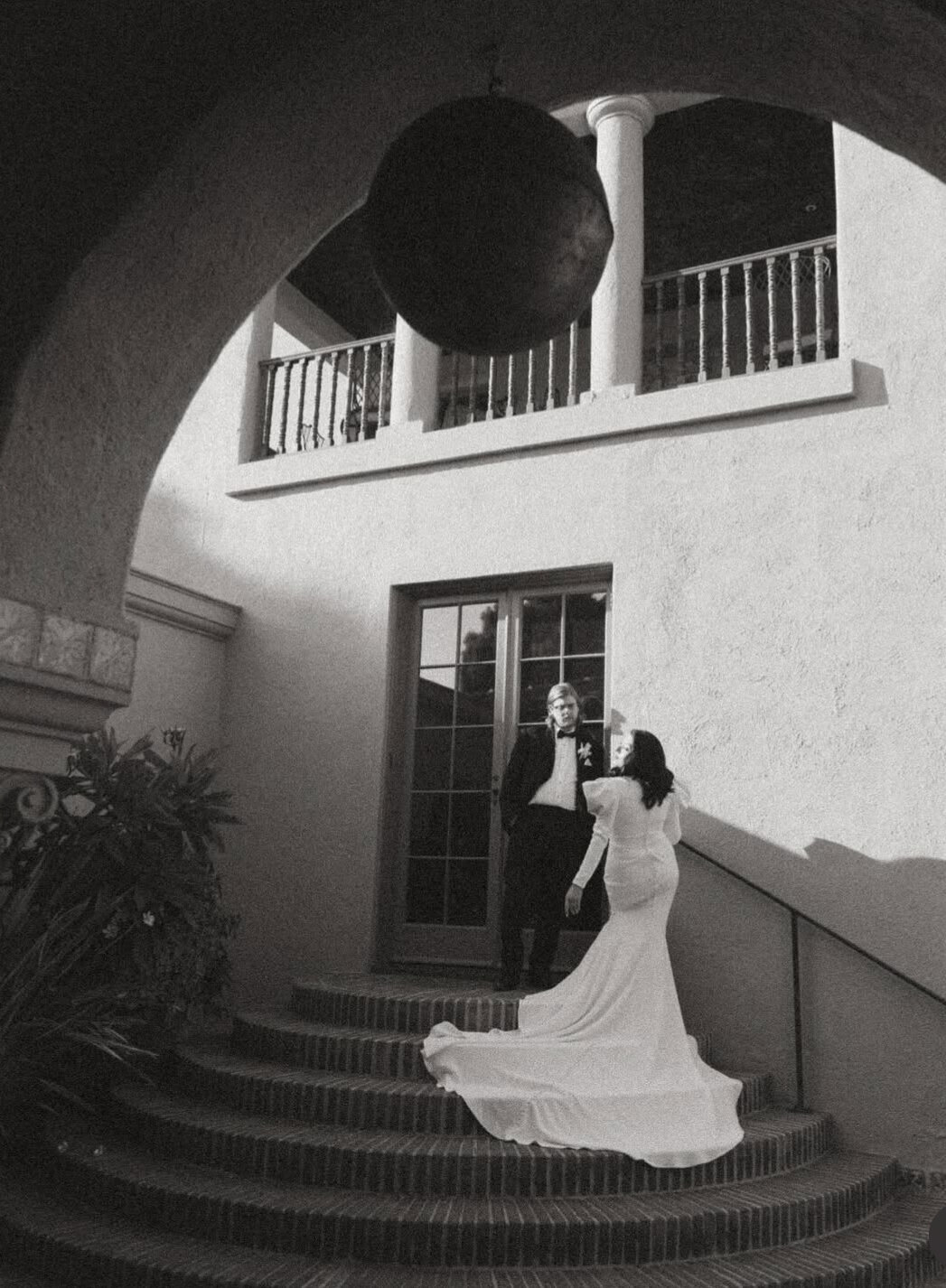 Bride and groom stand on a small staircase outside of a stucco building