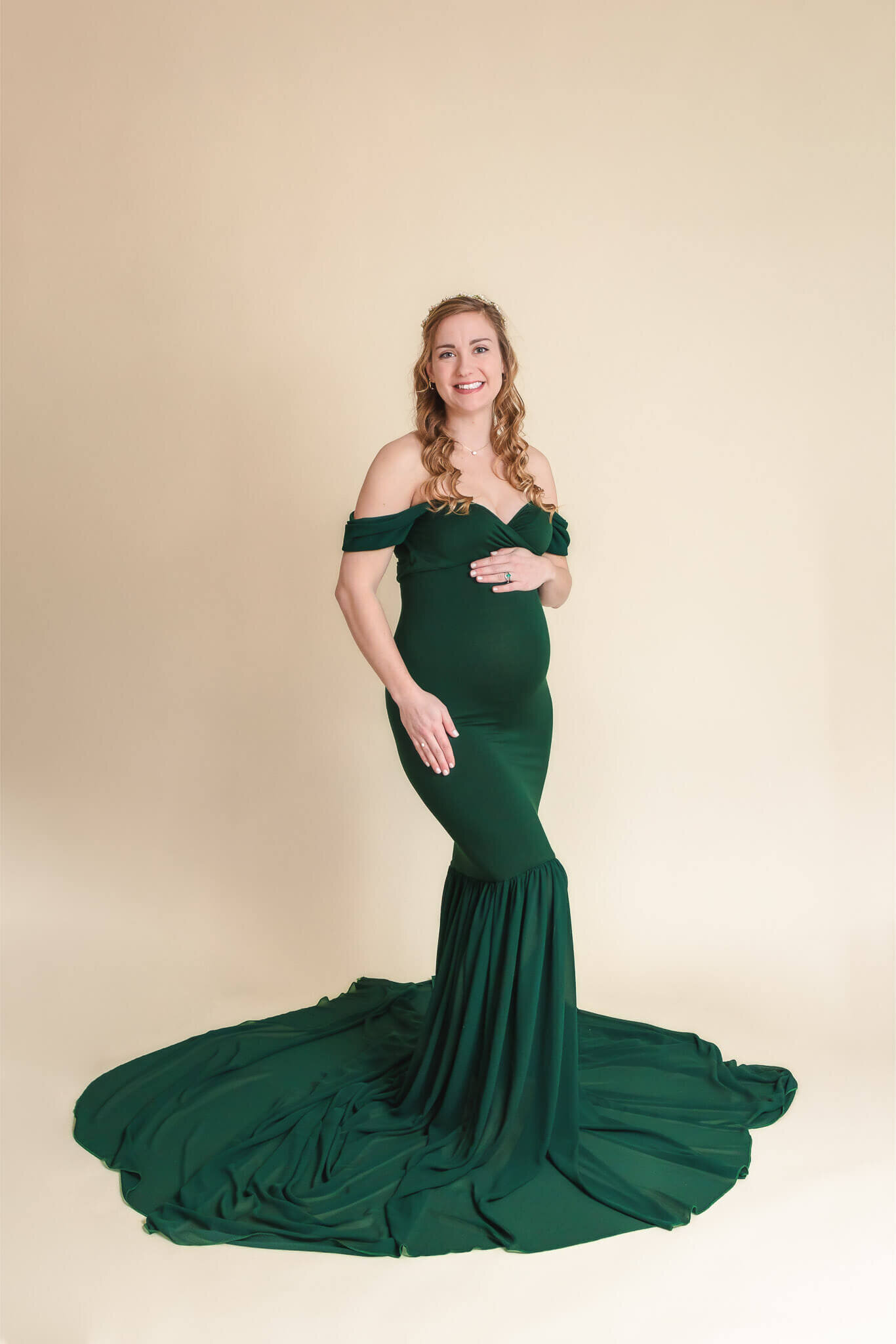 A pregnant woman in a green dress on a cream backdrop.