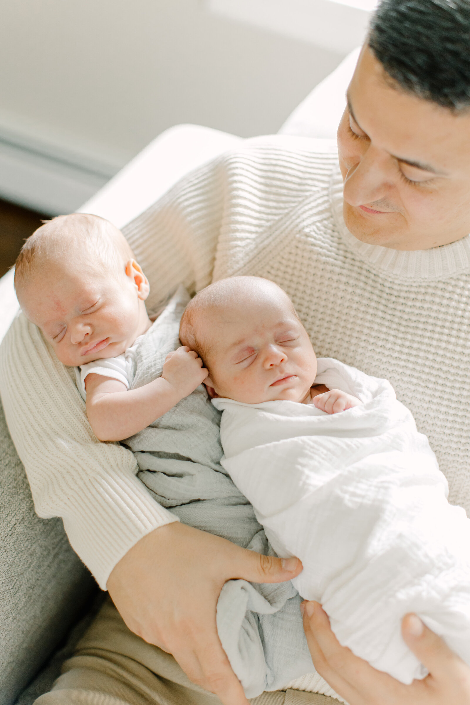 A father is holding his newborn twins swaddled in his arms