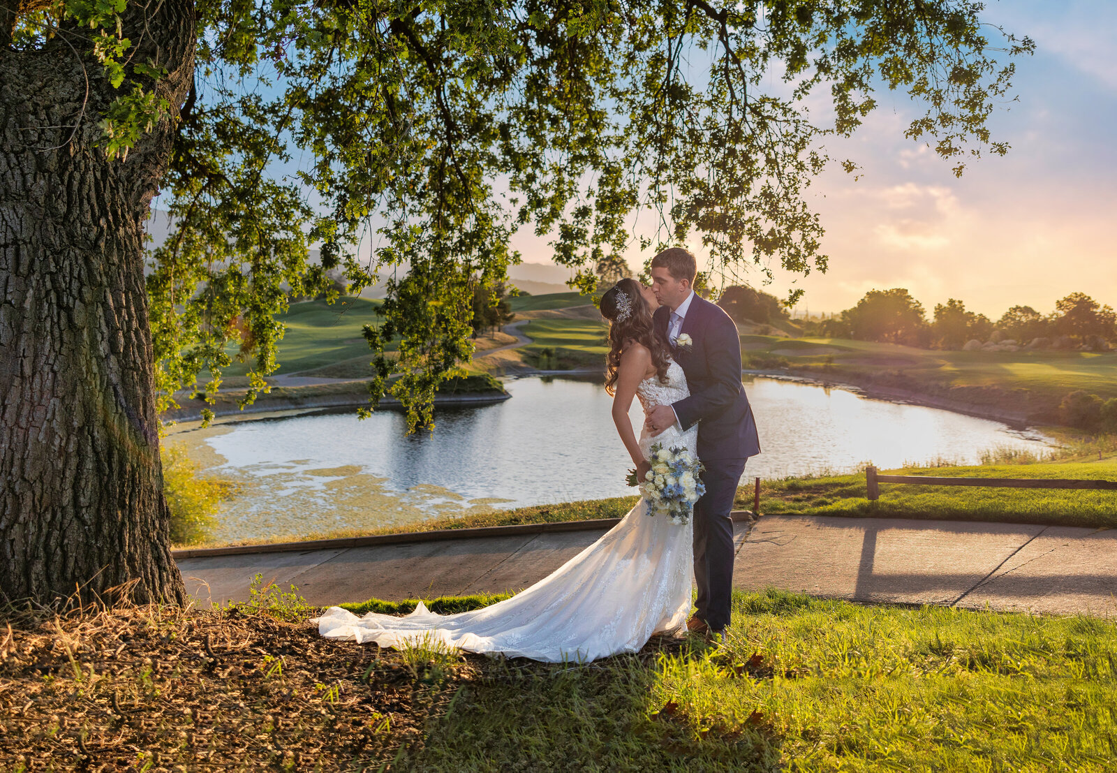 Bride and groom kiss under a willow tree with lake in the background with sunset. Photo by philippe studio pro, sacramento wedding photographer.