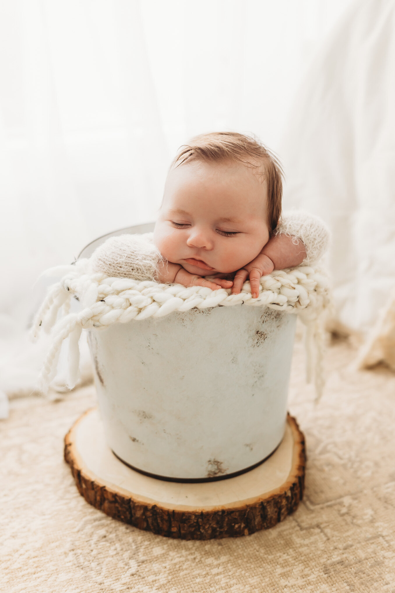 Newborn boy with beautiful hair sleeping with his head on his hands in a white bucket
