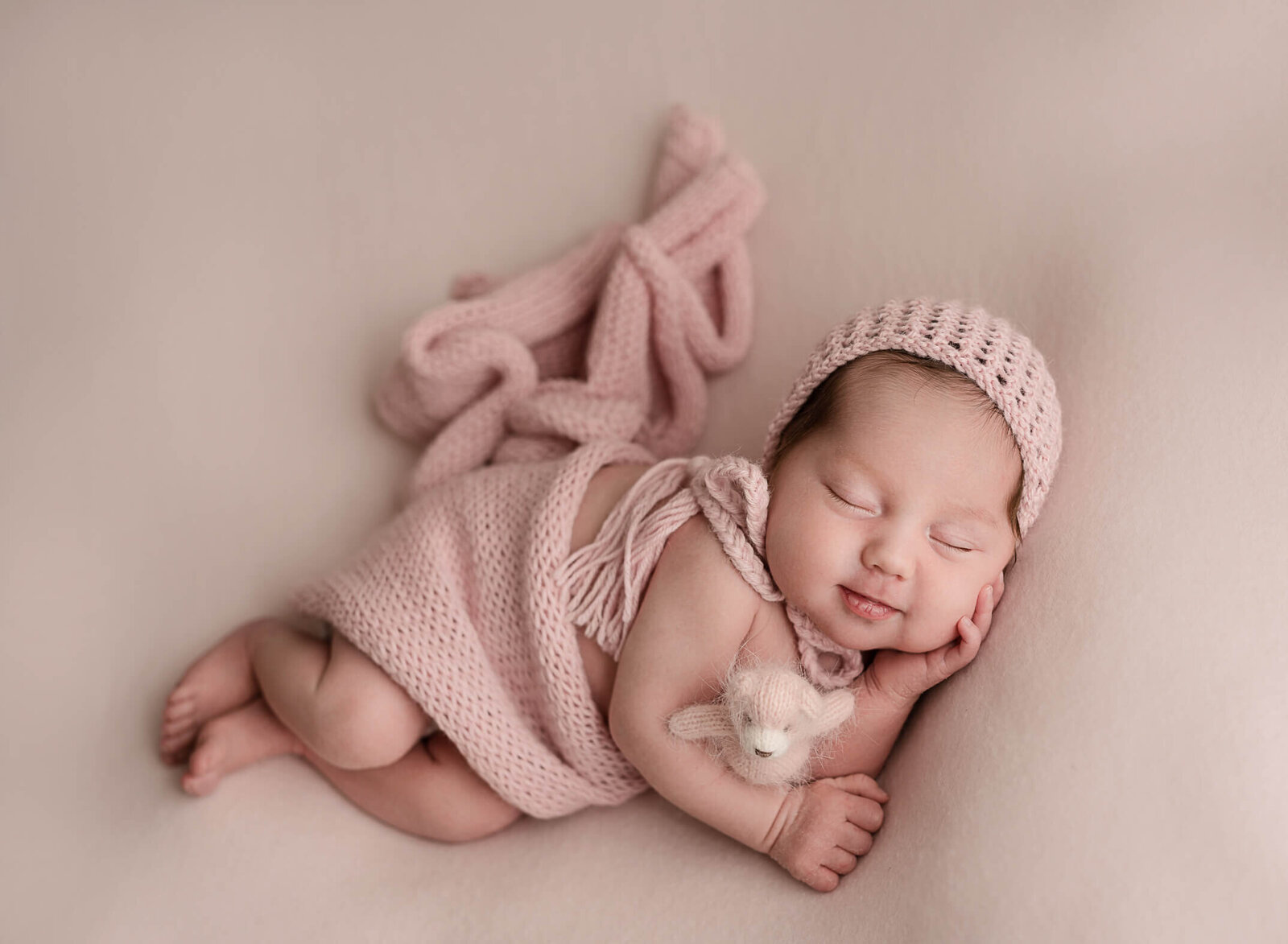 beautiful newborn baby girl laying in pink backdrop wearing a pink bonnet.  Photographed by mariela Duval Photography in Atlanta, Ga