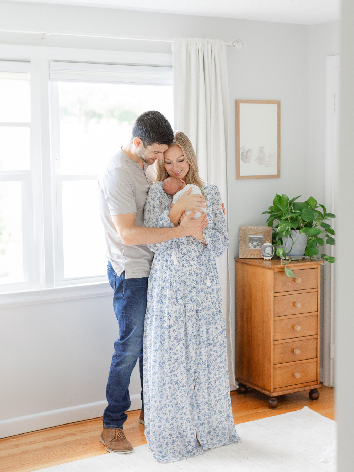 massachusetts mom wearing floral dress holds newborn baby while dad wraps his arms around her during boston in home newborn session