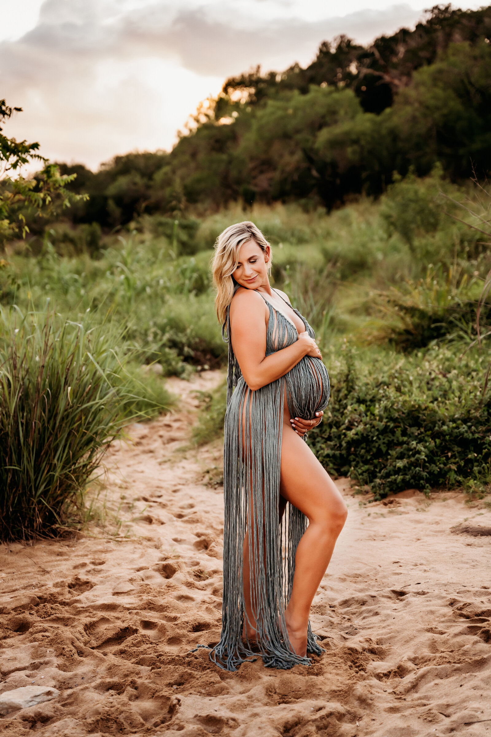 Maternity Photographer, a pregnant woman in lacy dress stands in the sand near lush vegetation