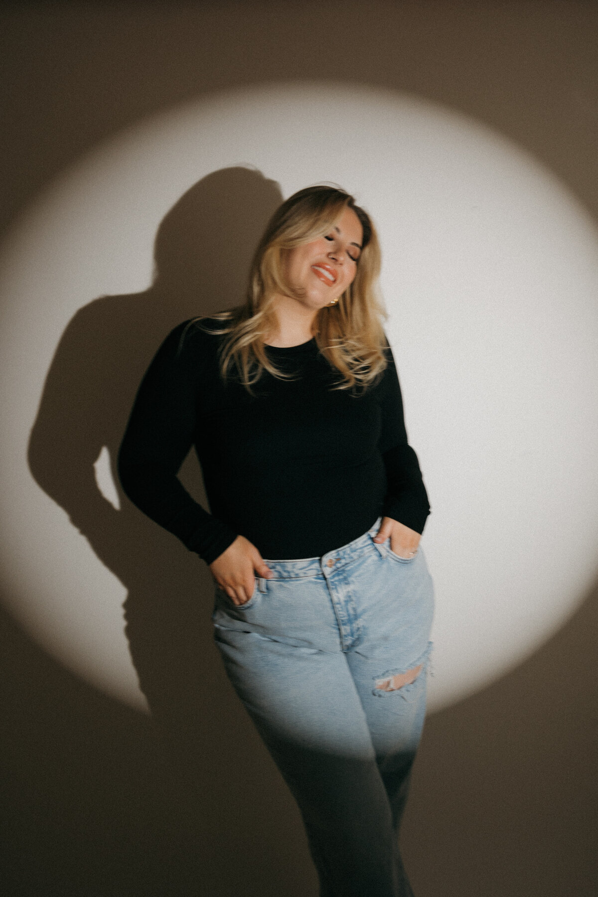Portrait of photographer Tarah Shea in spotlight with relaxed, editorial pose, West Coast wedding photographer branding image