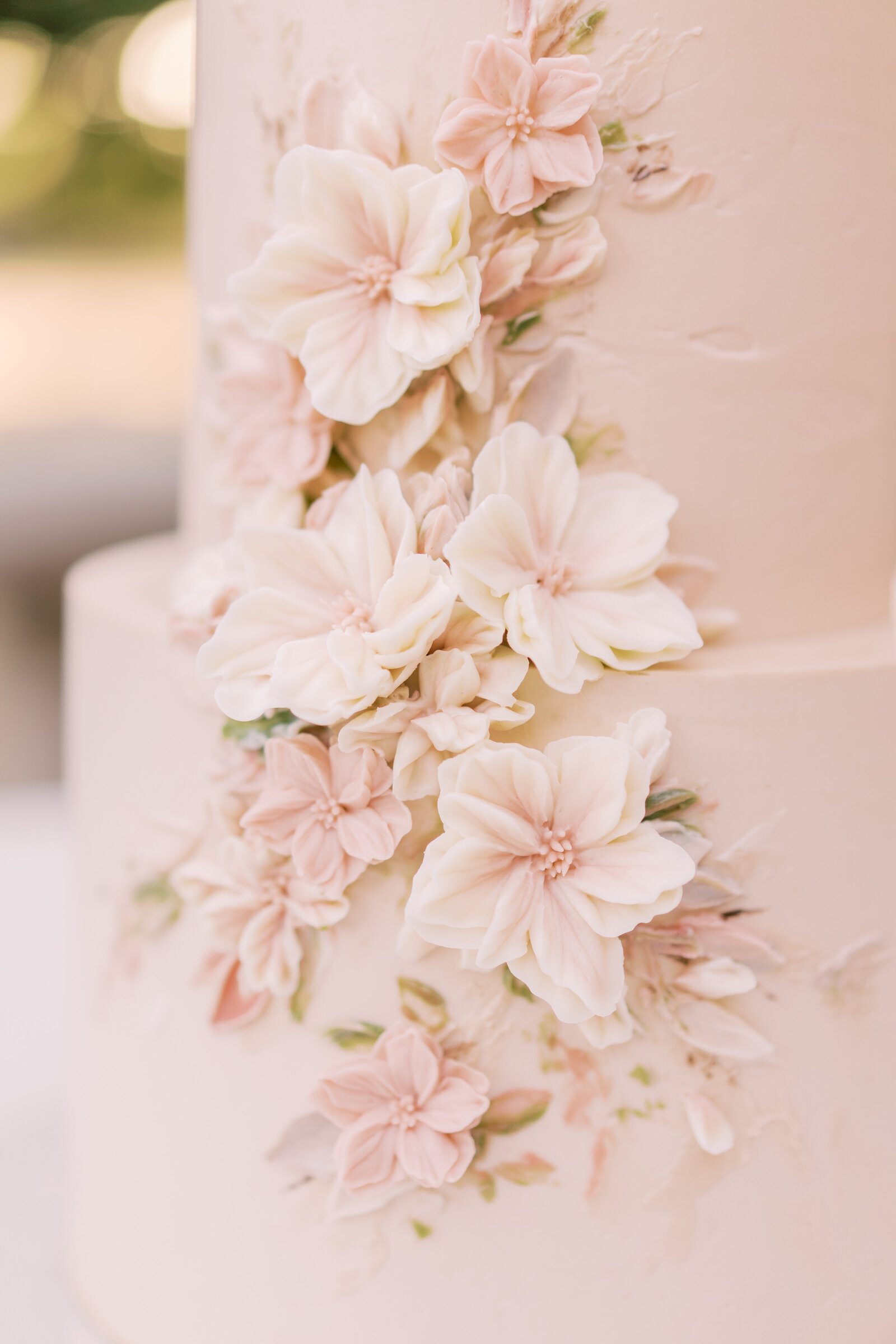 Portrait of a blush-colored wedding cake with blush flowers.
