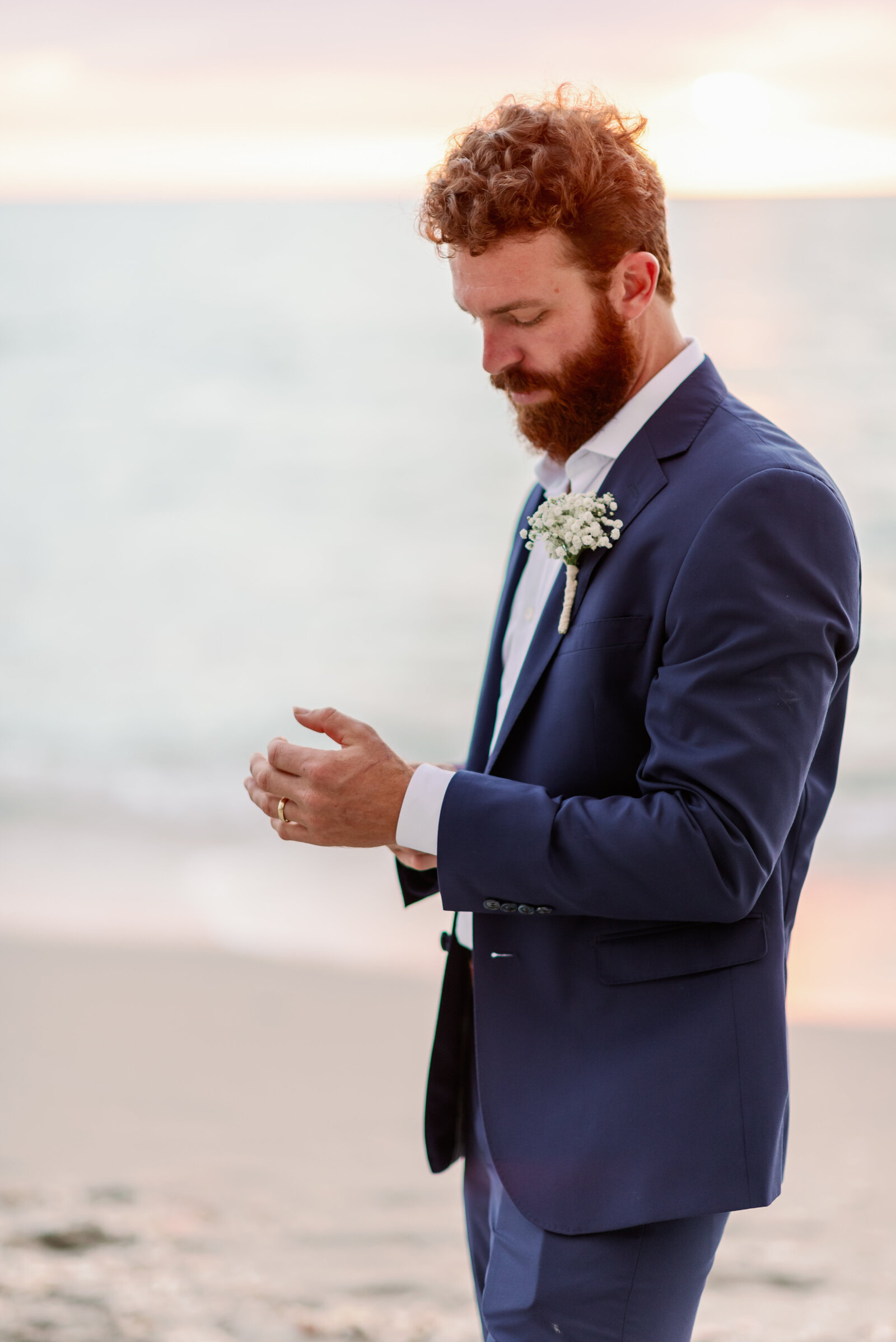 groom slone standing on the beach looking down at his wrist while he adjusts his watch