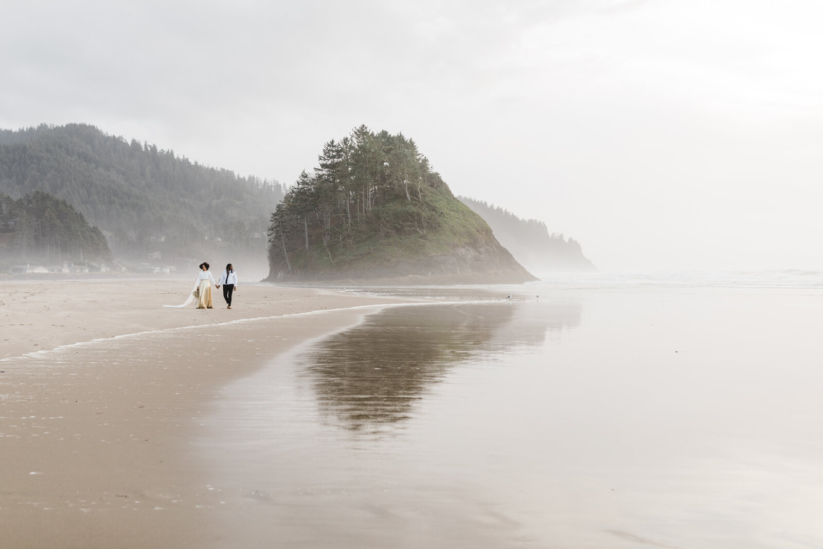 BIPOC couple strolls hand in hand along the sandy beach of the Pacific Ocean for their Oregon Coast adventure elopement in Neskowin. | Erica Swantek Photography