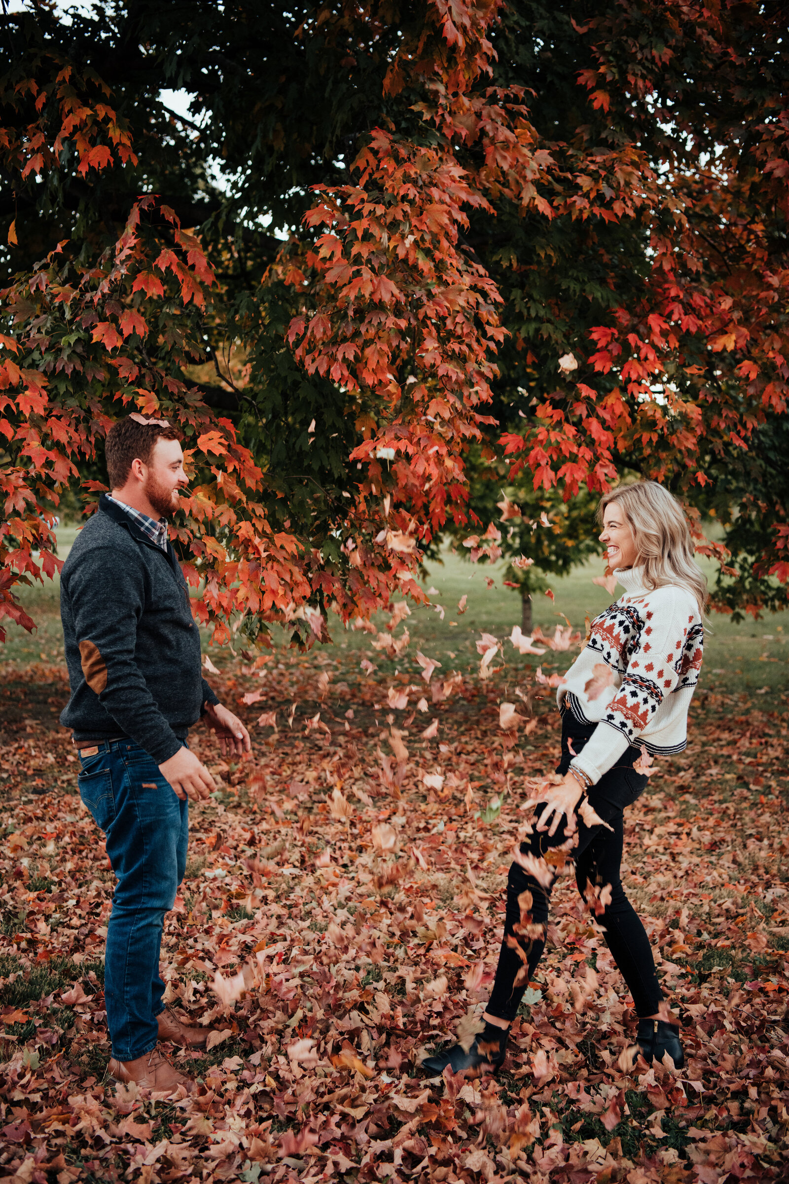 Engaged couple throwing fall leaves