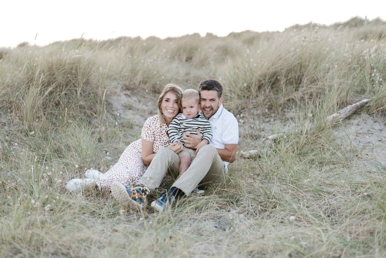 Mum and dad sitting on the sand with their son smiling in billingshurst family photoshoot