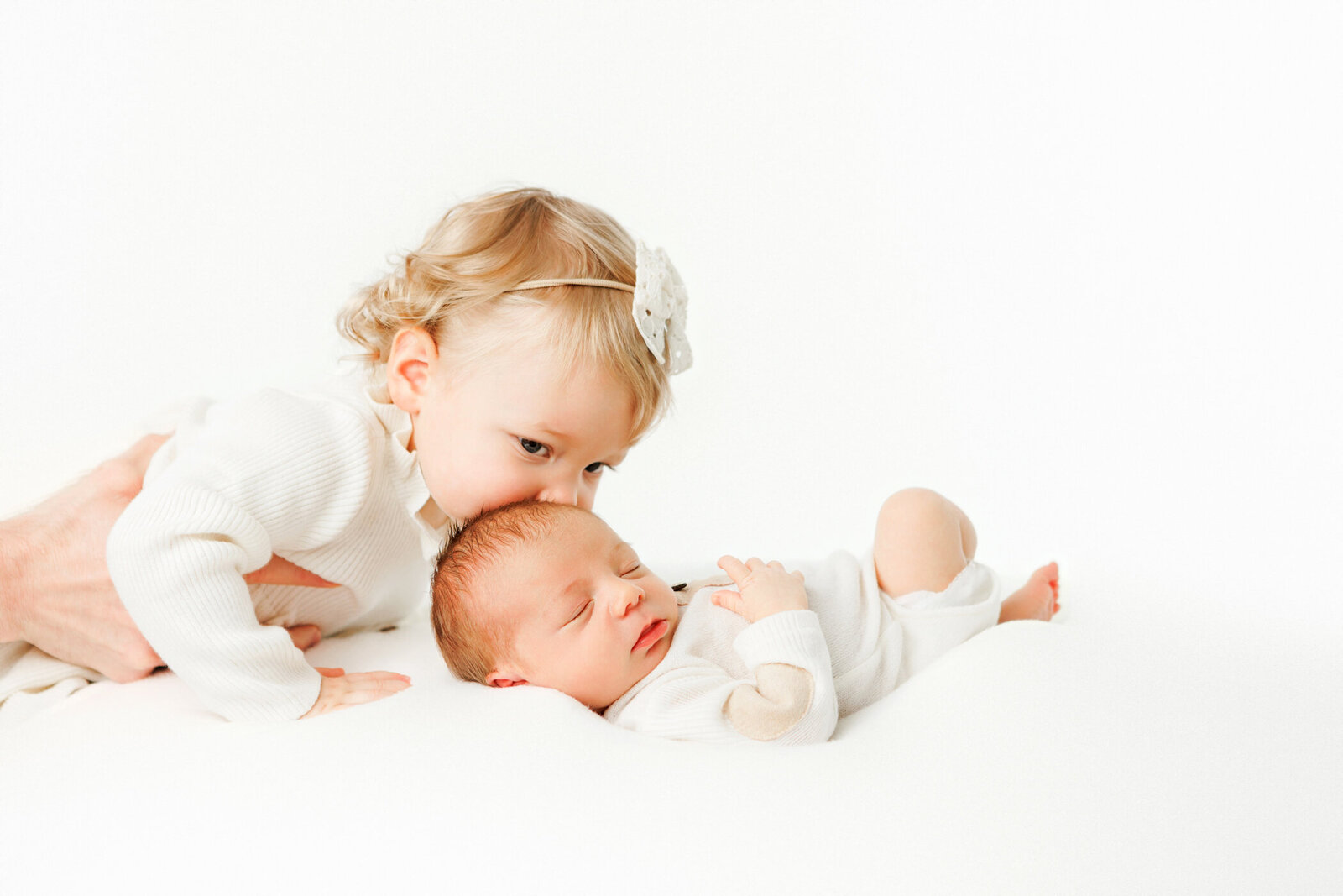 big sister kissing newborn baby boy on forehead, all white clothing, white background, fresno clovis, photographer