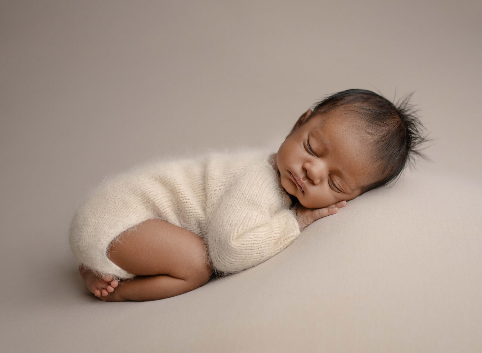 Baby wearing a cream romper and sleeping on his belly. Newborn Photography session photographed at Jenni Nikki's photo studio in Marietta, GA.