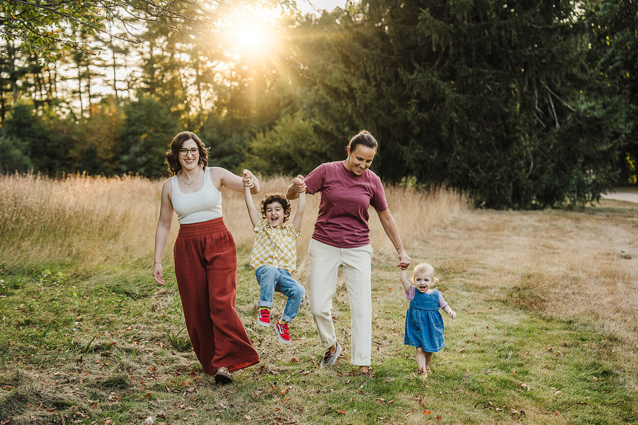 two moms swing their children between arms in a field at sunset