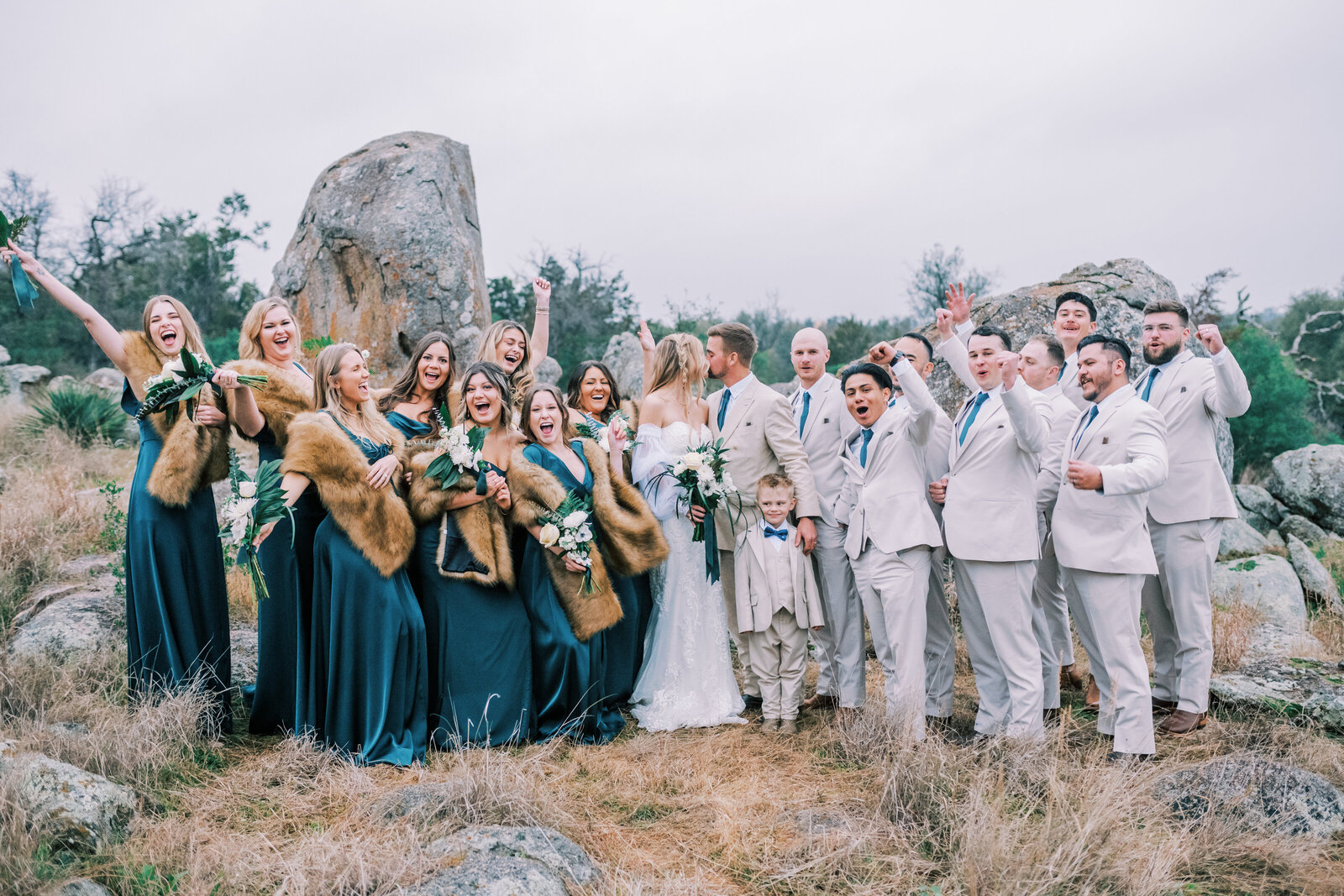 Bridal party standing outside and cheering while bride and groom kiss