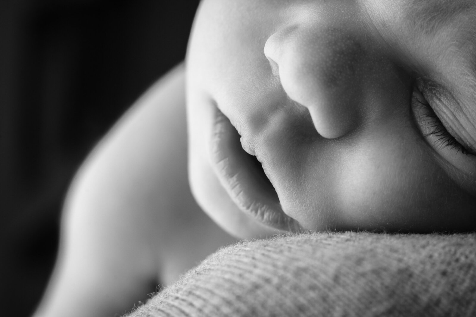A close-up of a sleeping newborn baby’s face, captured in black and white. The image focuses on the peaceful expression and delicate features of the baby.