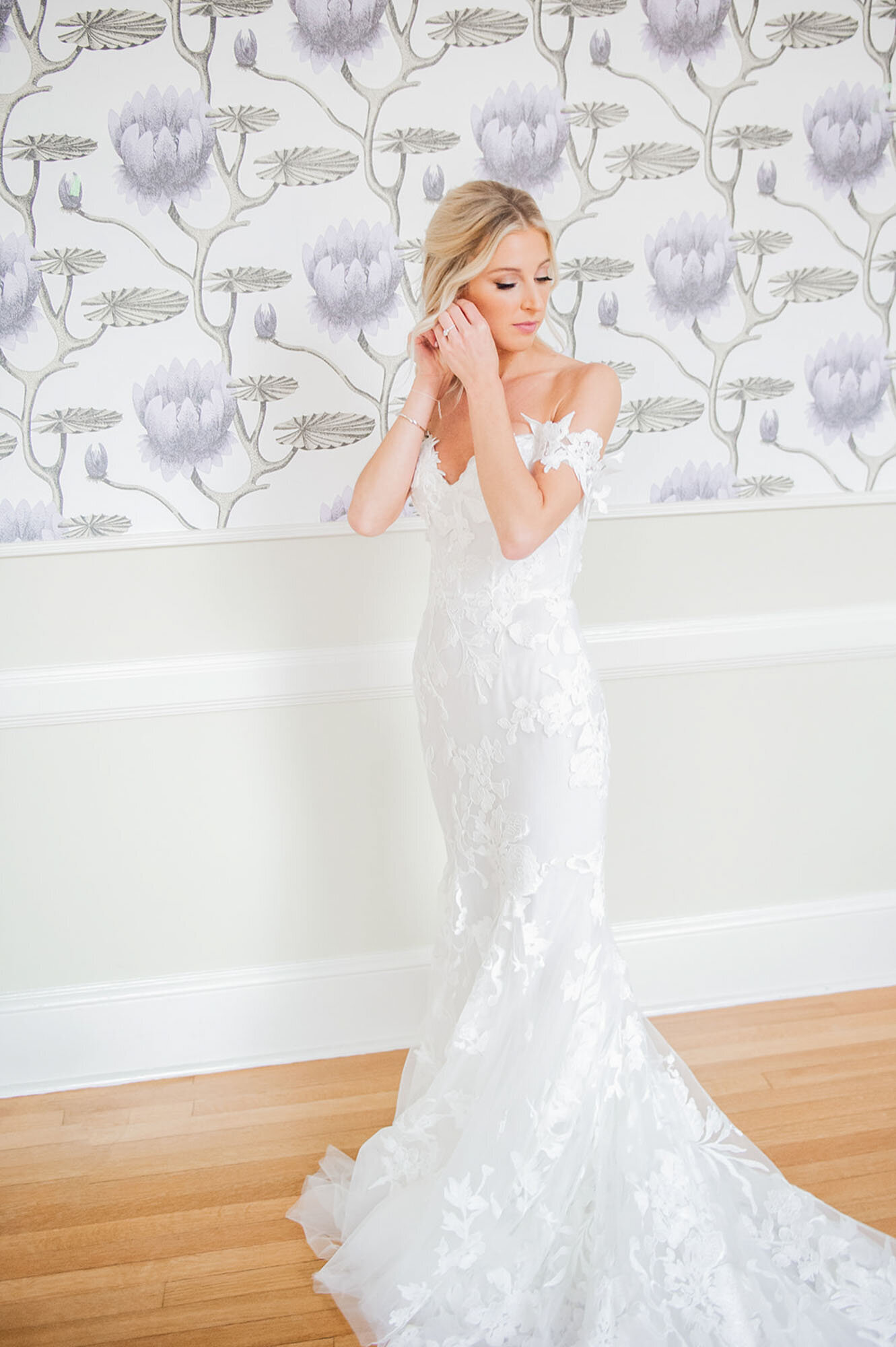 bride putting on earrings in front of floral wallpaper