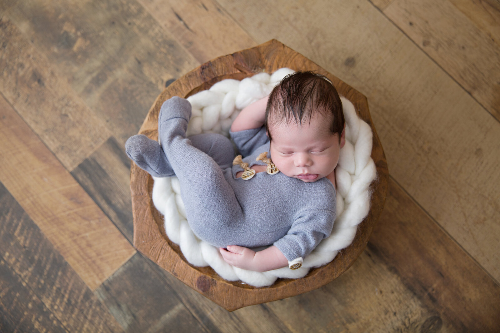 sleeping newborn baby in blue sleeper posed in wooden bowl