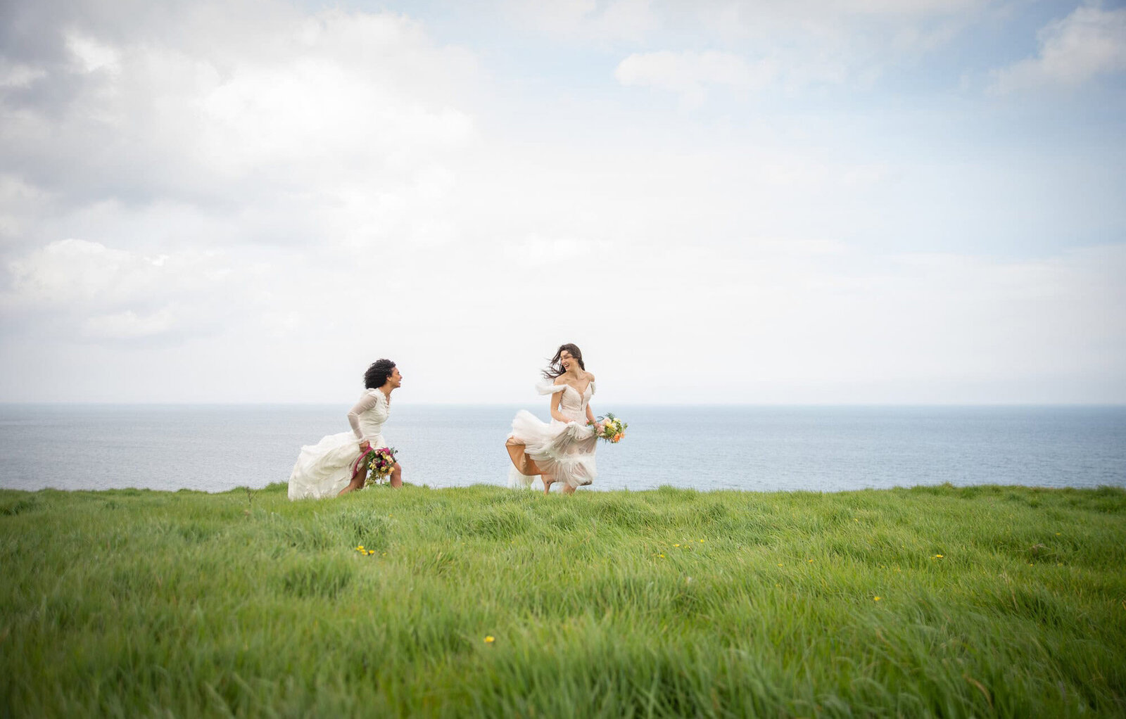 brides run in grass with sea in the background