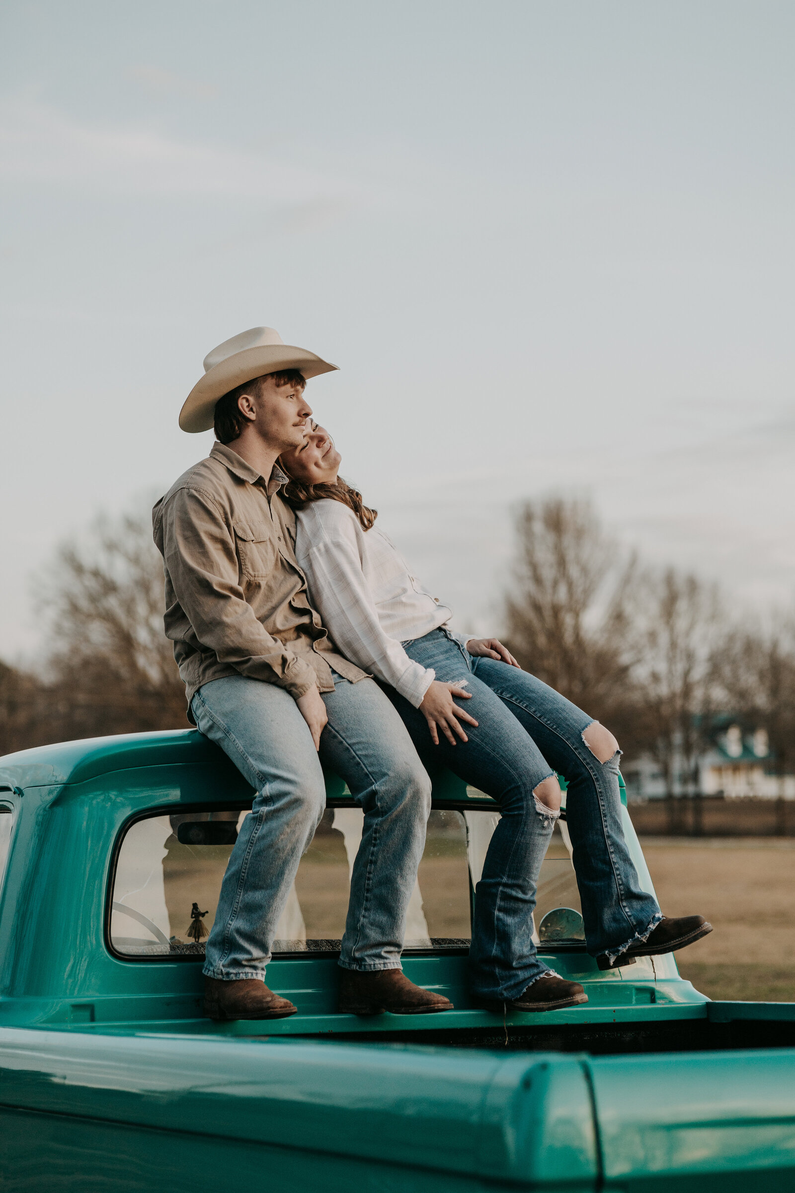 Couple sitting atop a vintage truck, watching the sunset. Romantic, rustic vibe.