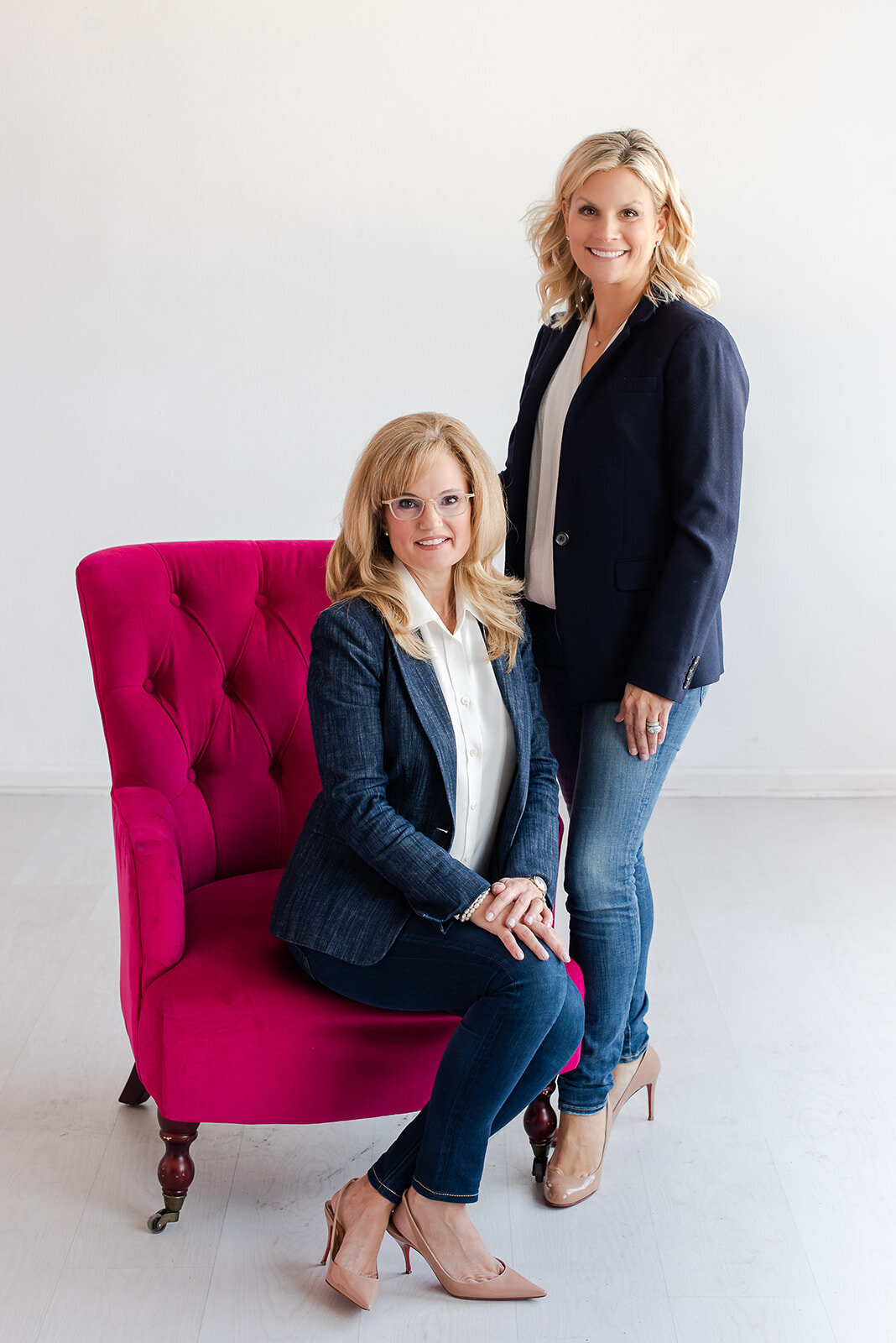 Modern headshot for two females one sitting on pink chair one standing