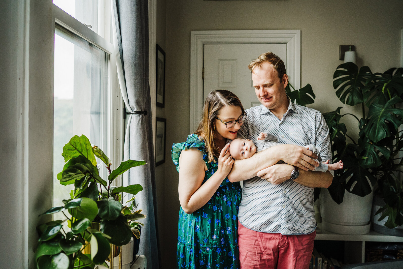 parents admire newborn in apartment filled with plants