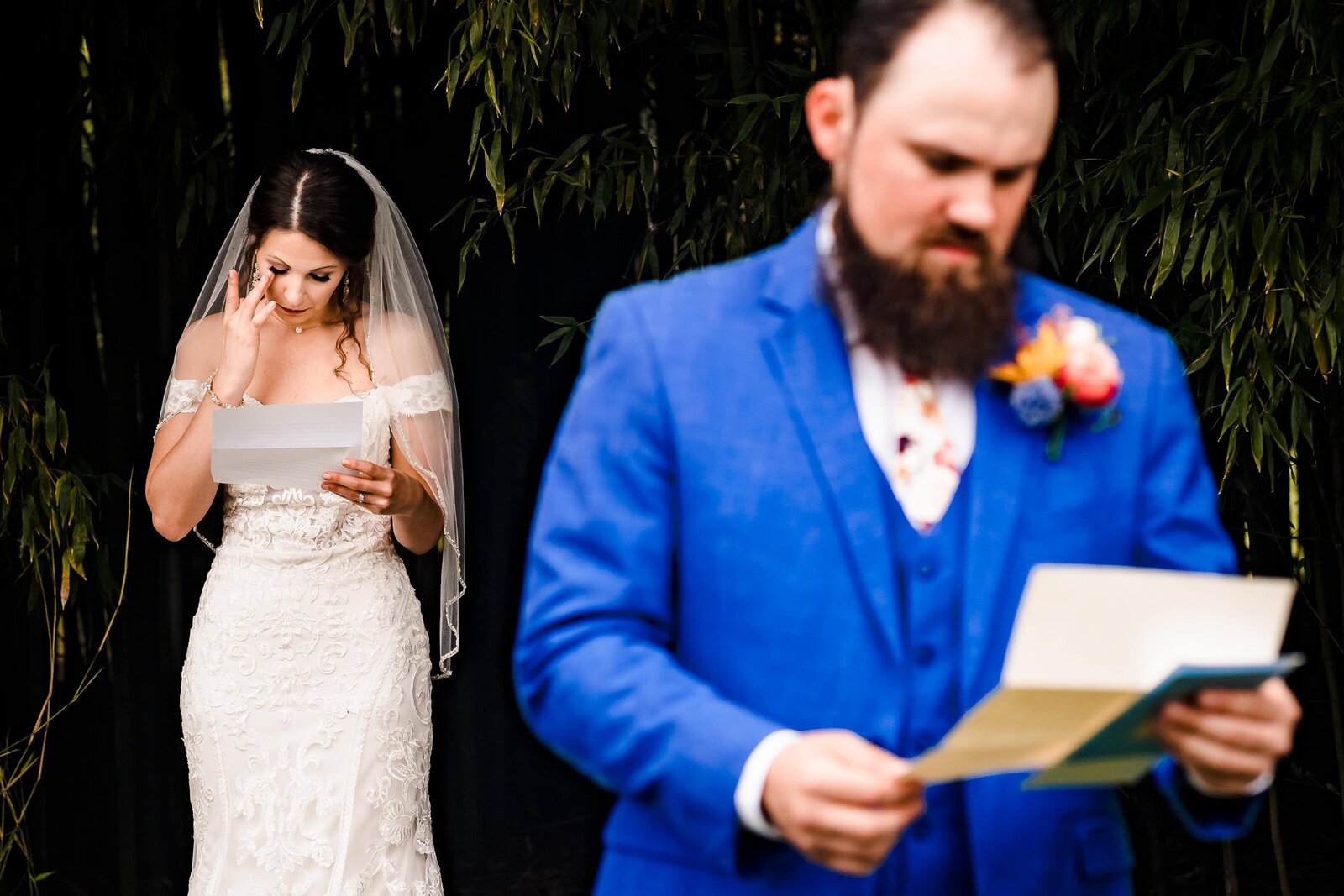 bride wipes away a tear as she reads a letter from the groom; in the foreground the groom is reading a letter from the bride