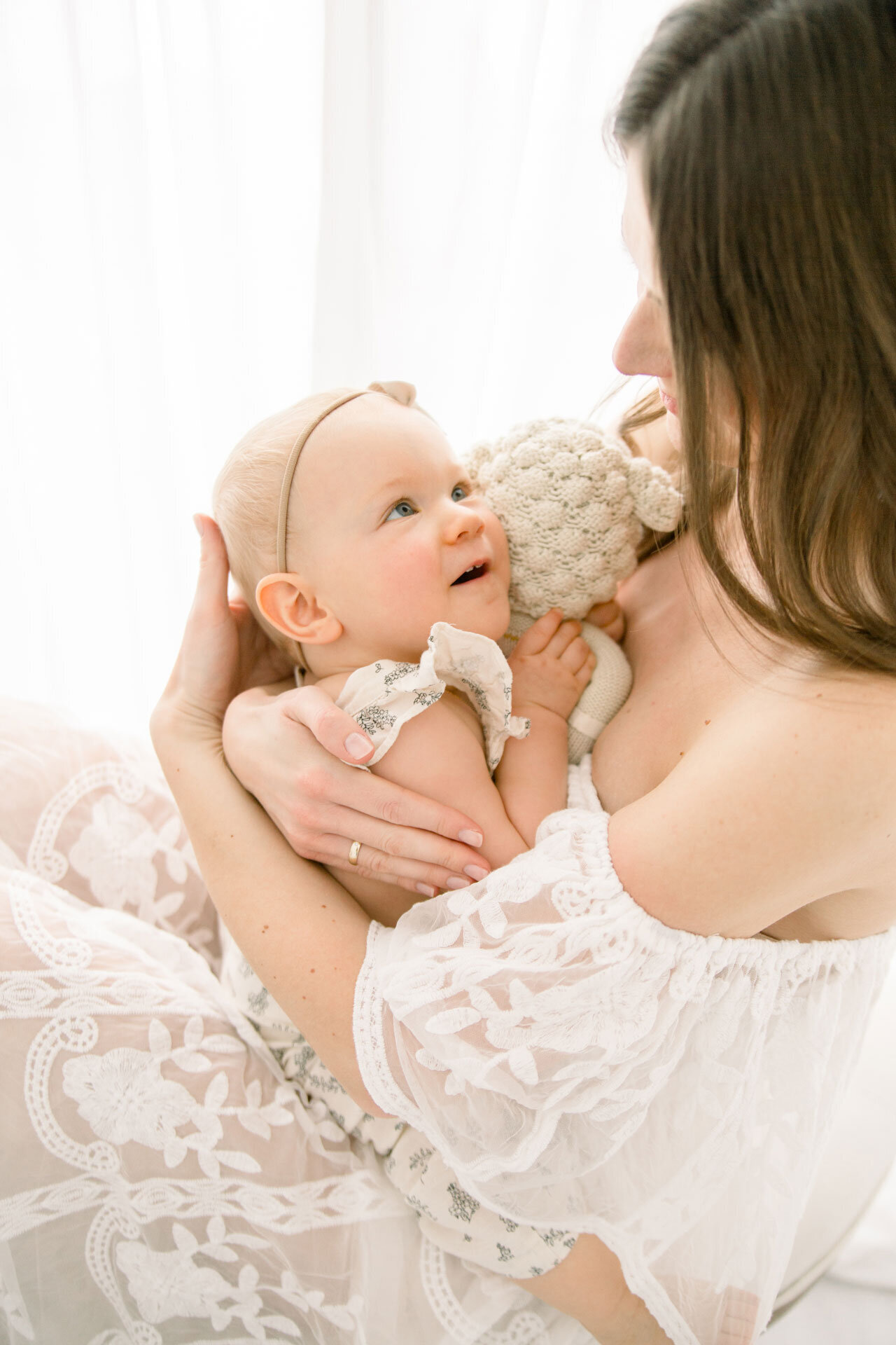 Babyfotografie Verl. mama im weißen Kleid hält Baby im Arm, das sie verliebt ansieht.