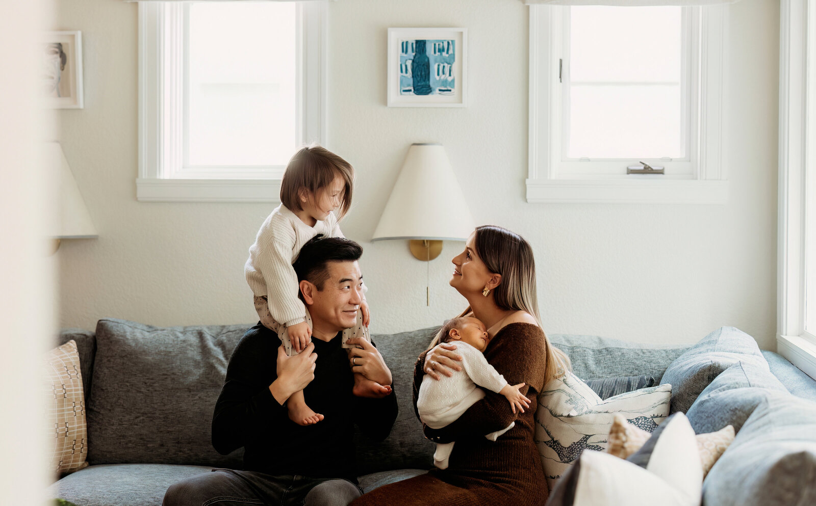 Family of four sitting on couch snuggling a newborn for an at home newborn session in Denver